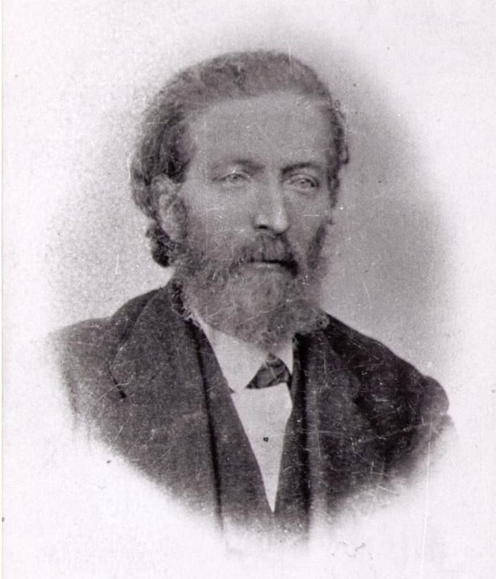 Black-and-white studio portrait of a bearded man in a suit, facing forward.