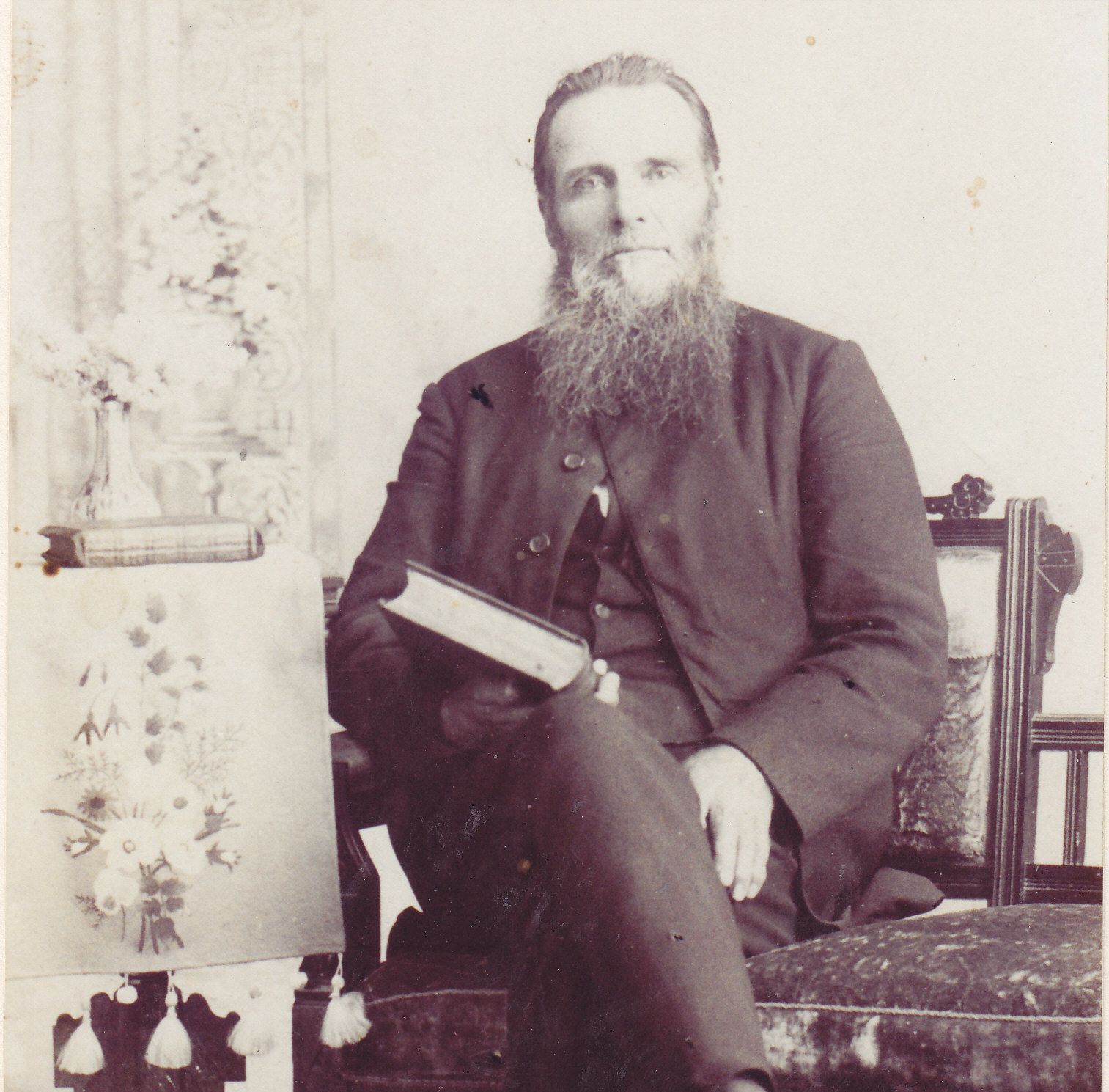 Sepia portrait of a bearded man seated with a book on his lap in a formal chair
