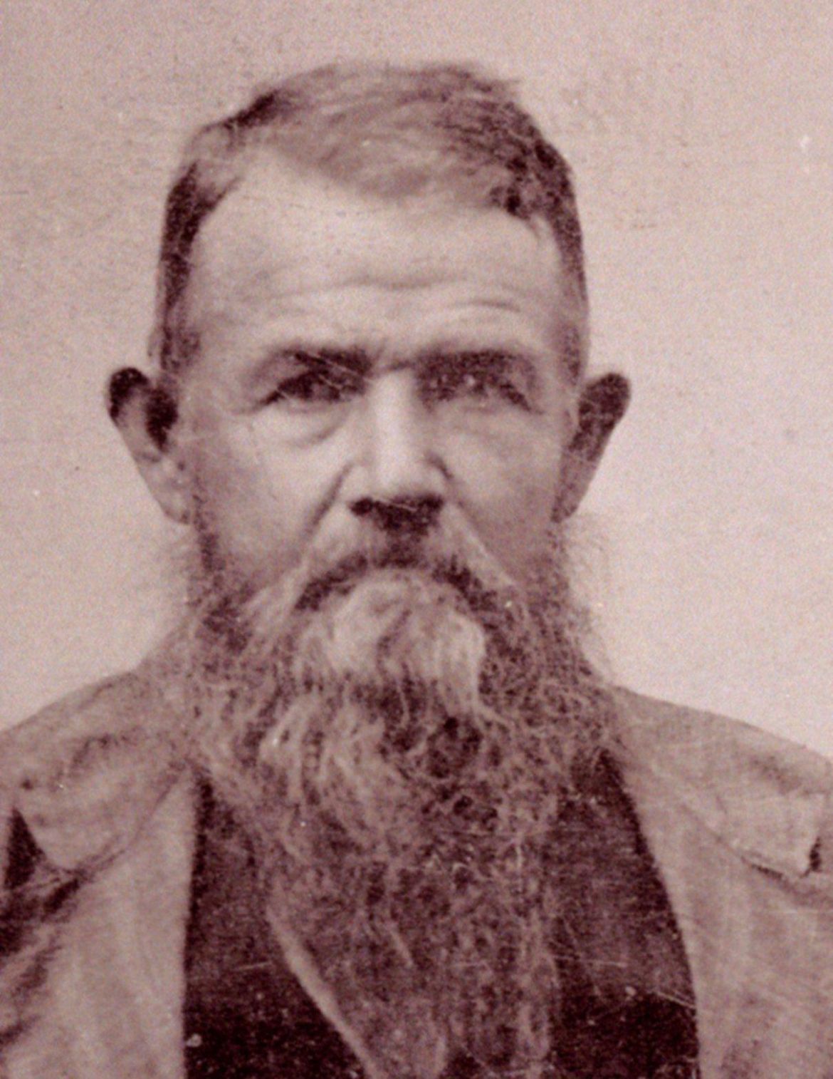 Sepia portrait of a stern man with a long beard, wearing a jacket.