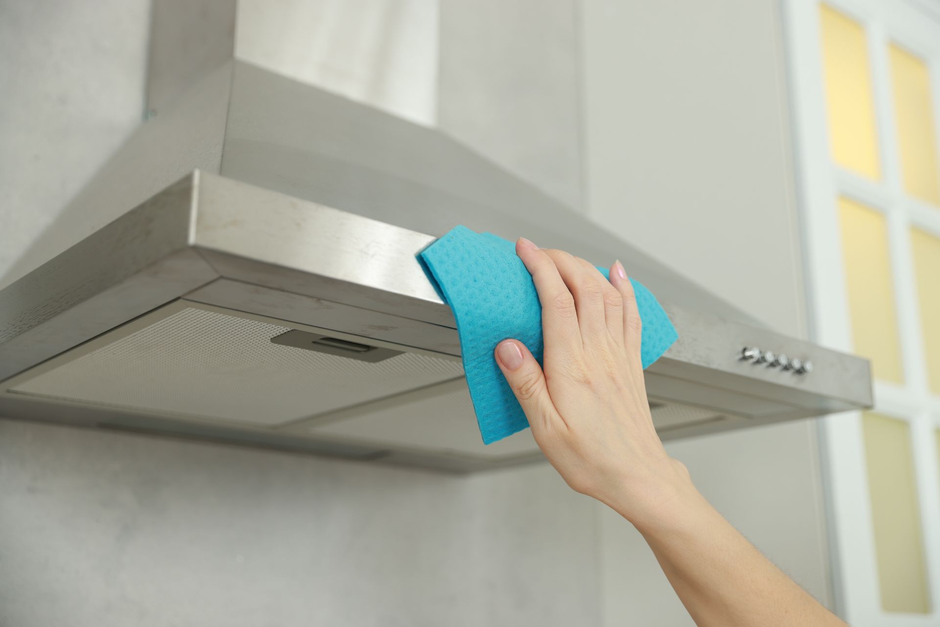 Hand wiping a blue cloth across a stainless steel range hood in a kitchen.