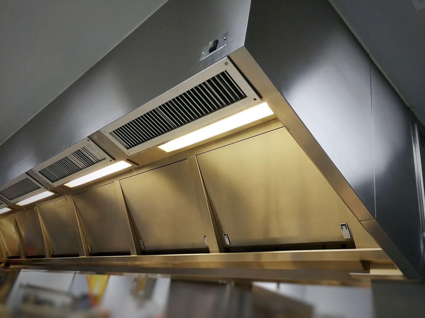 Stainless steel commercial kitchen exhaust hood with lights and filters.