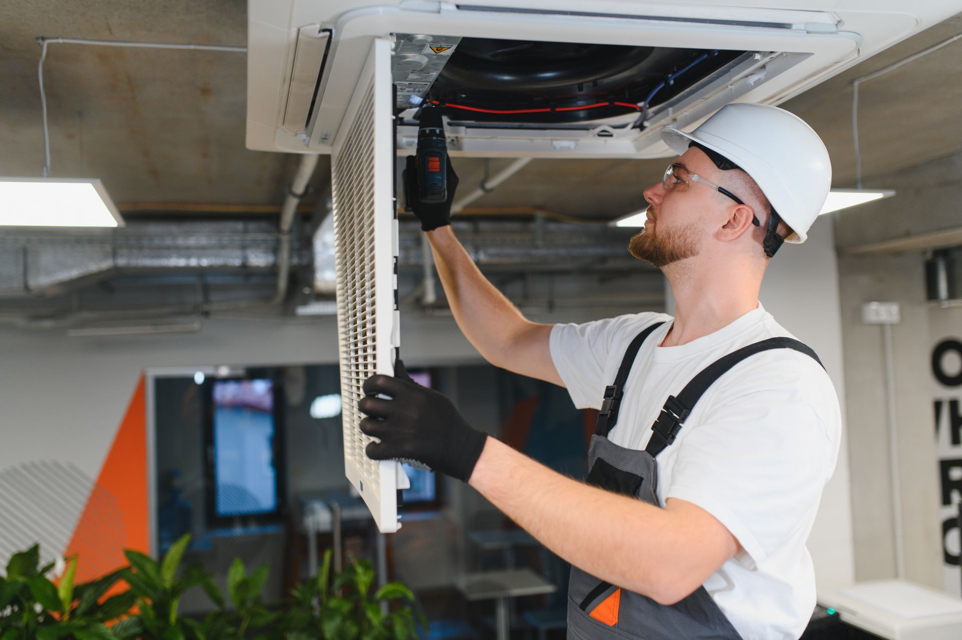 HVAC technician in a white hard hat and gloves servicing an air conditioning unit.