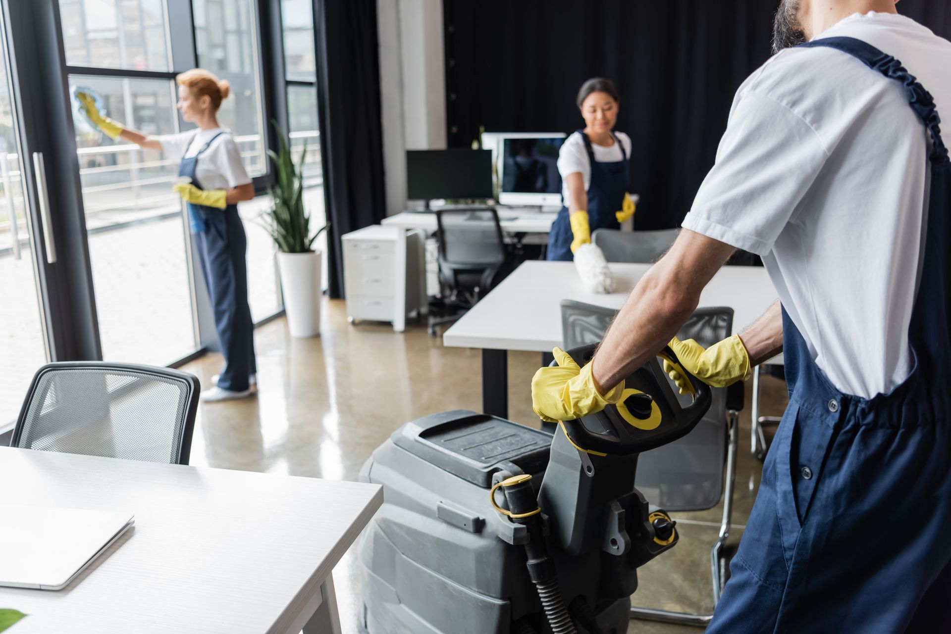 Office cleaners using equipment, wiping windows, and cleaning desks.