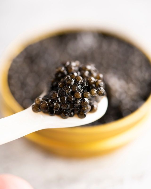 A person is holding a spoon full of caviar in front of a bowl of caviar.