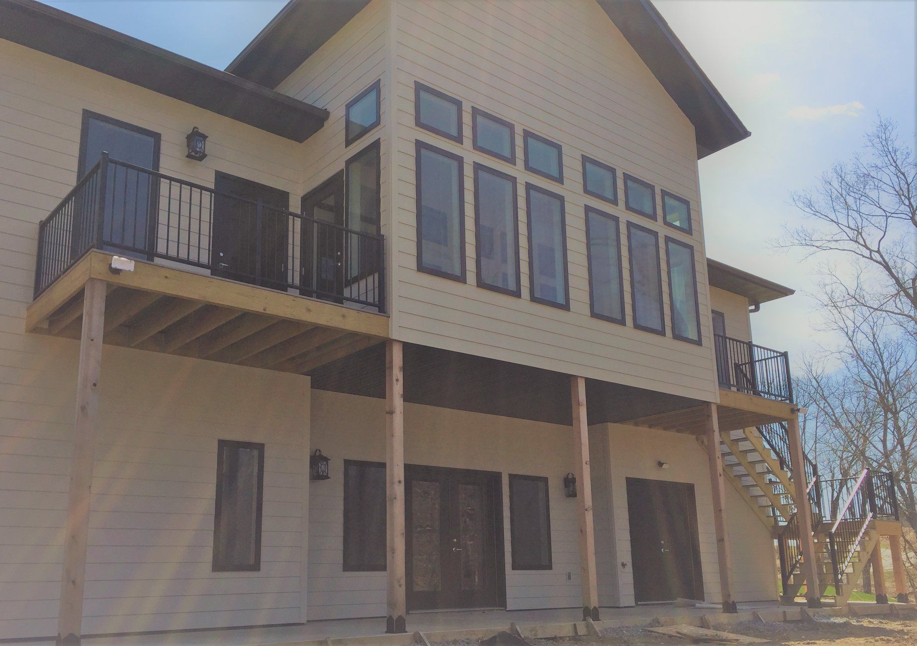 Two-story house with large windows, beige siding, and a second-floor balcony under a sloped roof.
