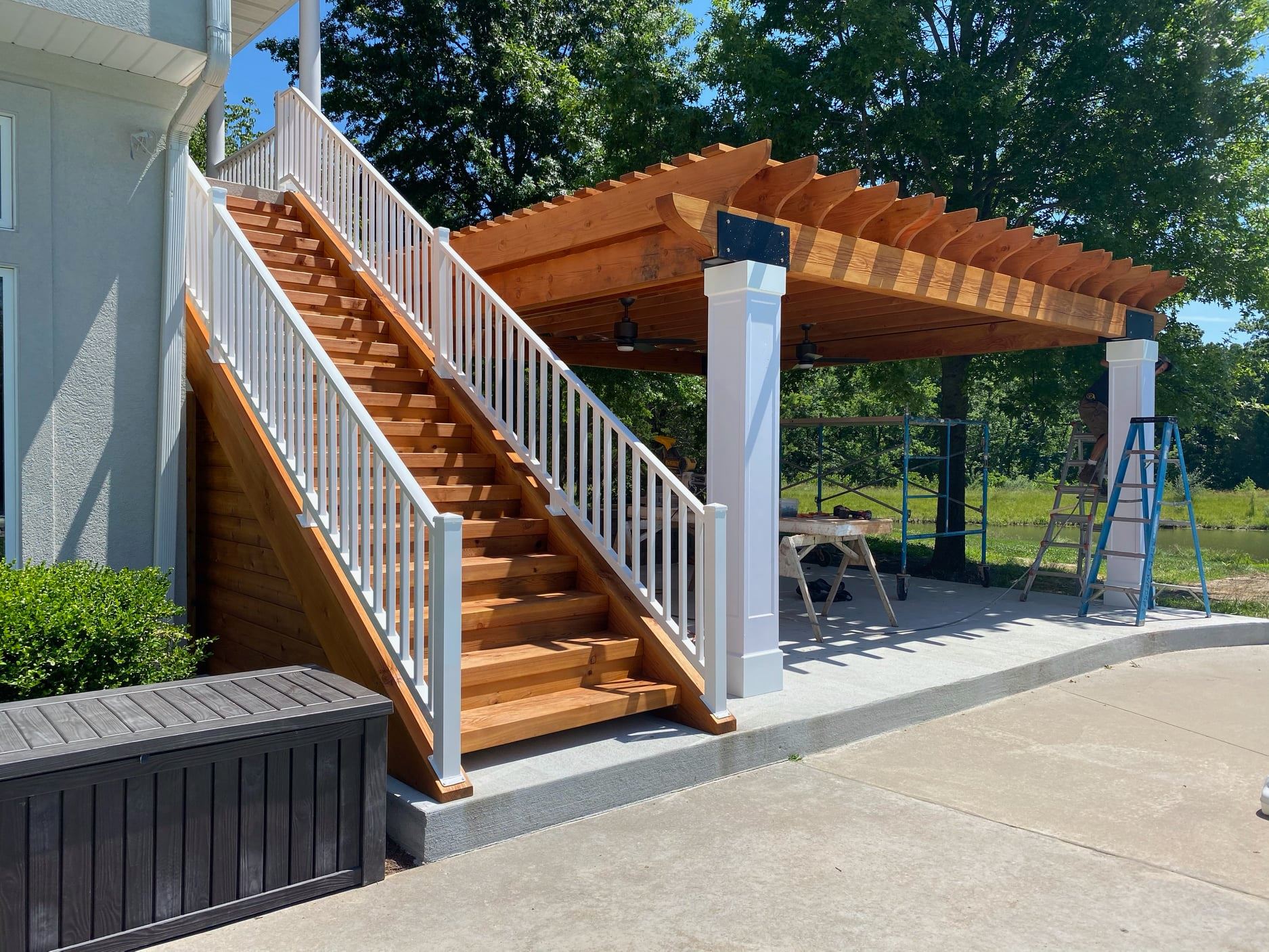 Outdoor wooden staircase beside a pergola-covered patio with white railings and columns