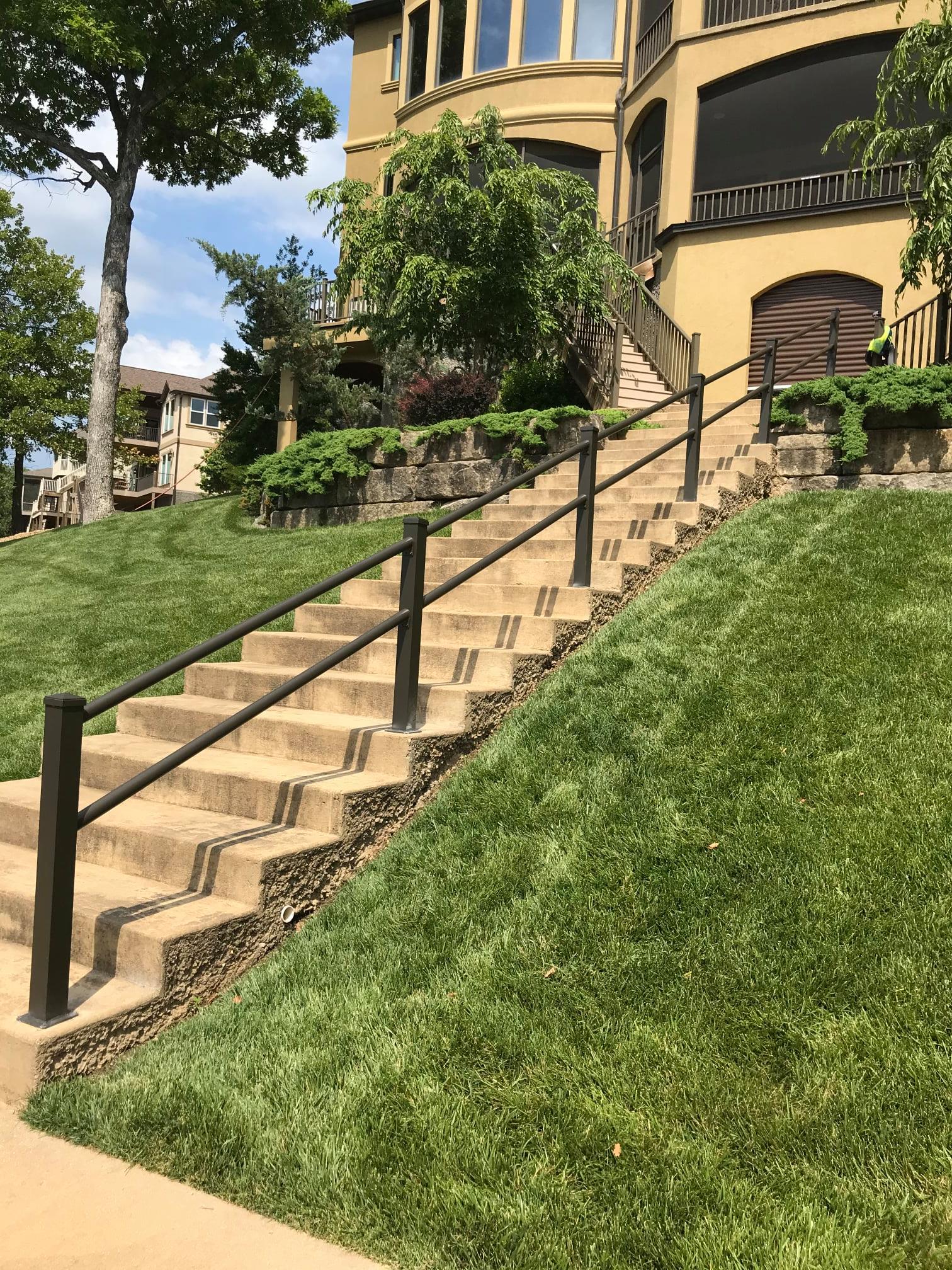 Stairway with black handrails beside a green grassy slope and tan building exterior.