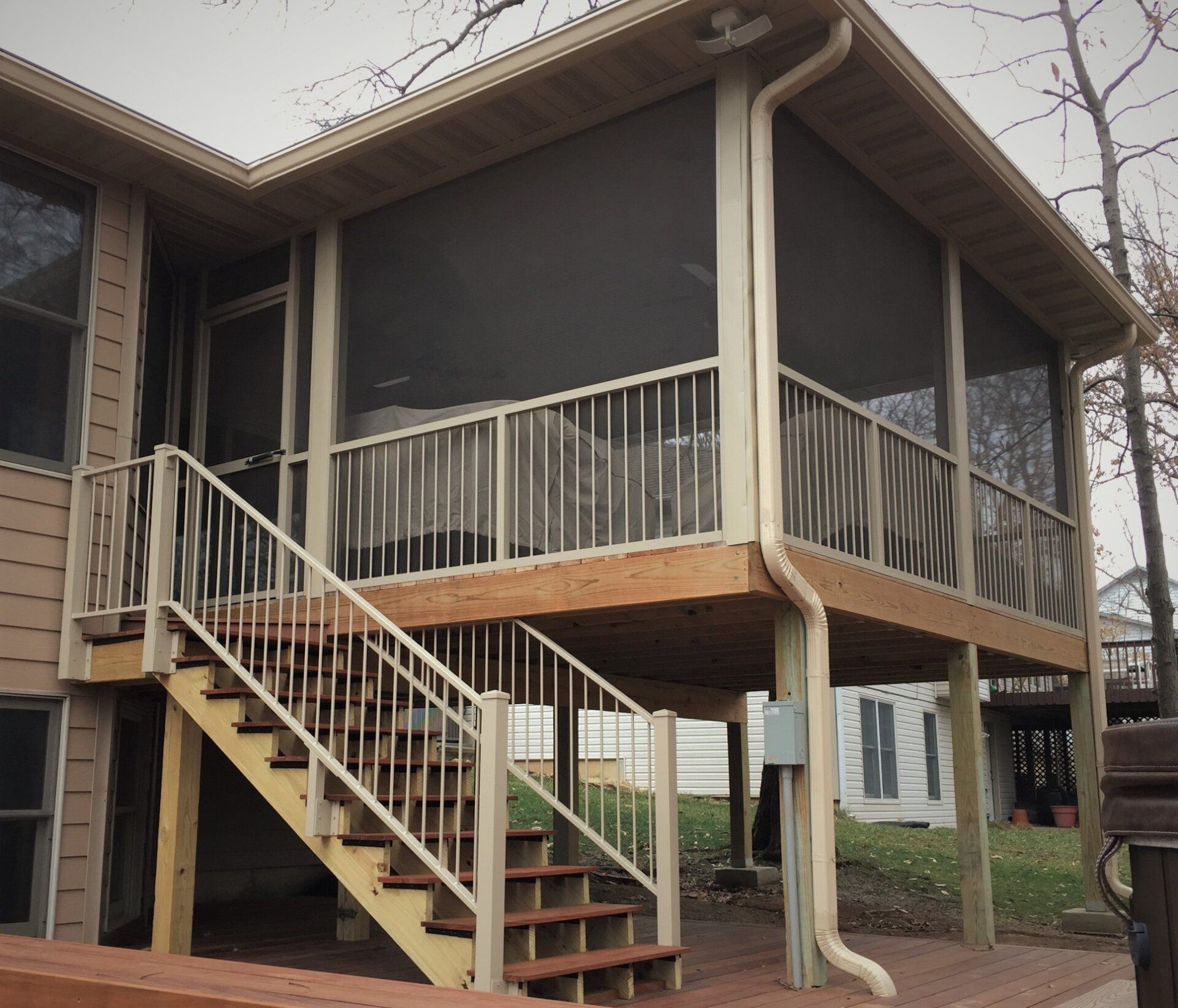 Elevated house porch with stairs, white railings, and screened-in deck under a gabled roof