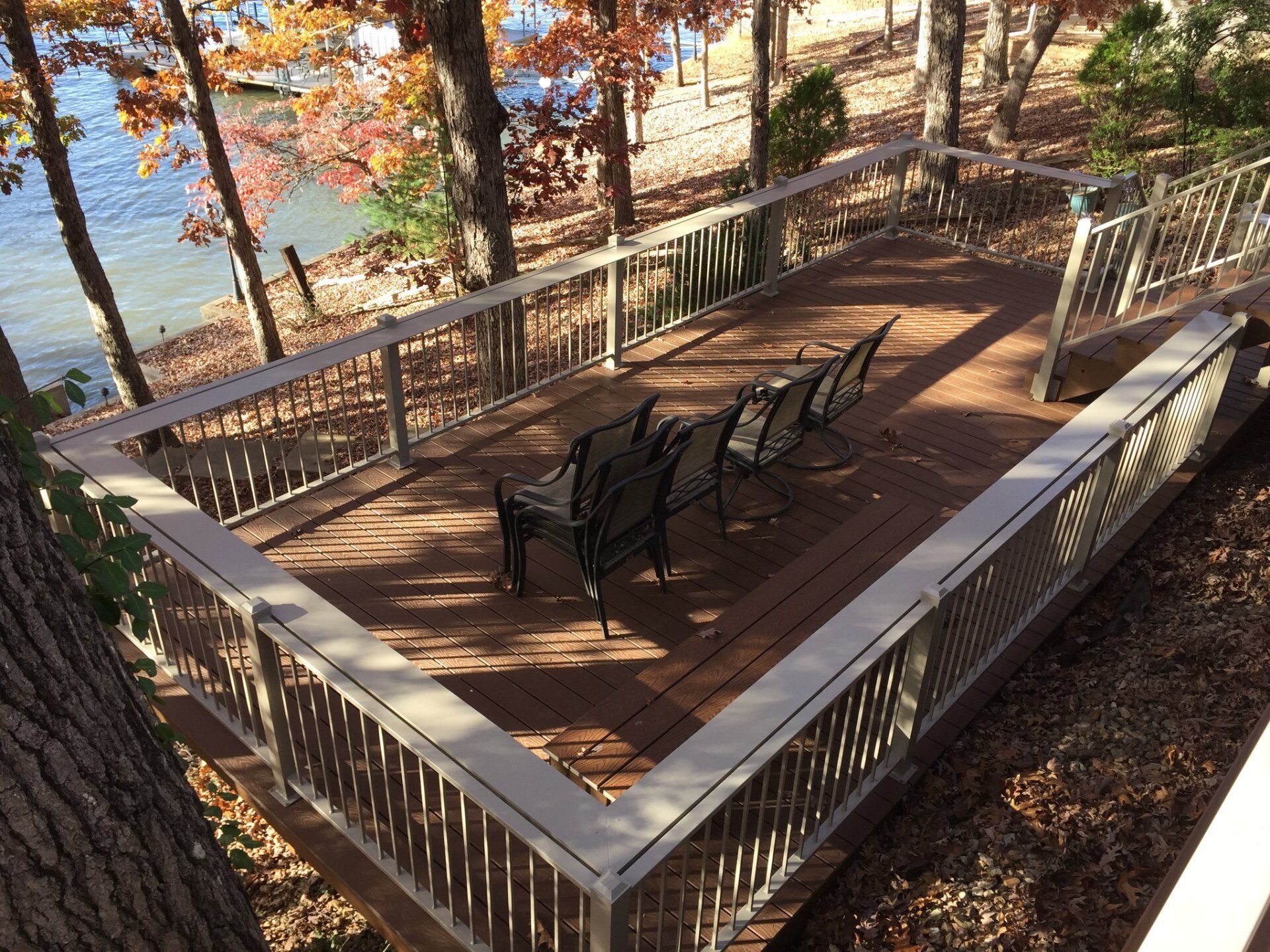 Wooden deck with chairs and a table overlooking a lake, surrounded by autumn trees