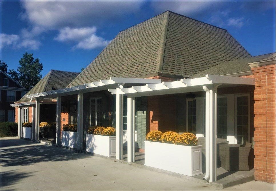 Storefront with flower boxes, white columns, and a shingled roof under a blue sky