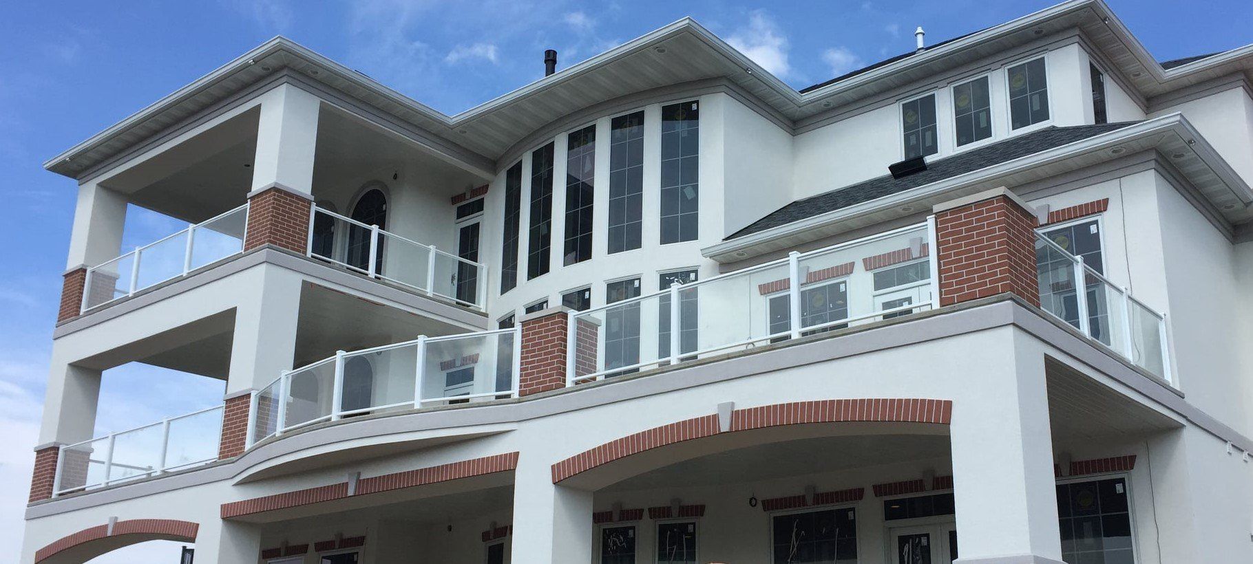 Modern multi-story house with white balconies, red brick accents, and arched front windows under a blue sky