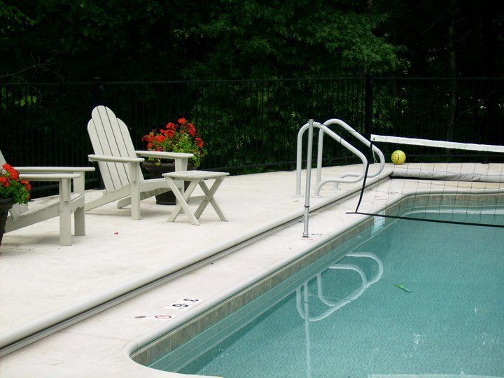 Poolside patio with white chairs and a handrail beside a turquoise swimming pool