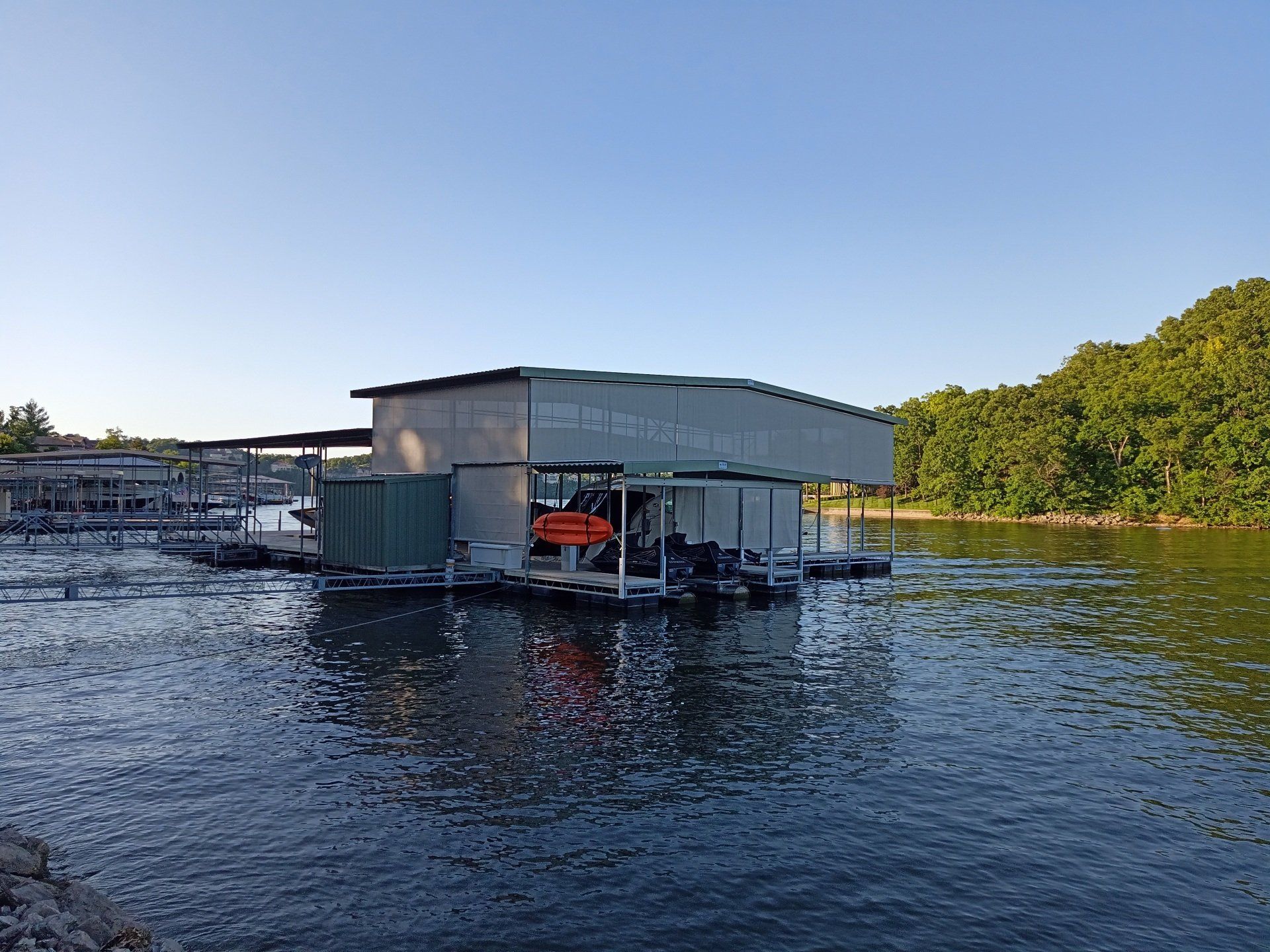 Floating boathouse with dock and orange life ring on calm water, trees along the shore under a clear sky