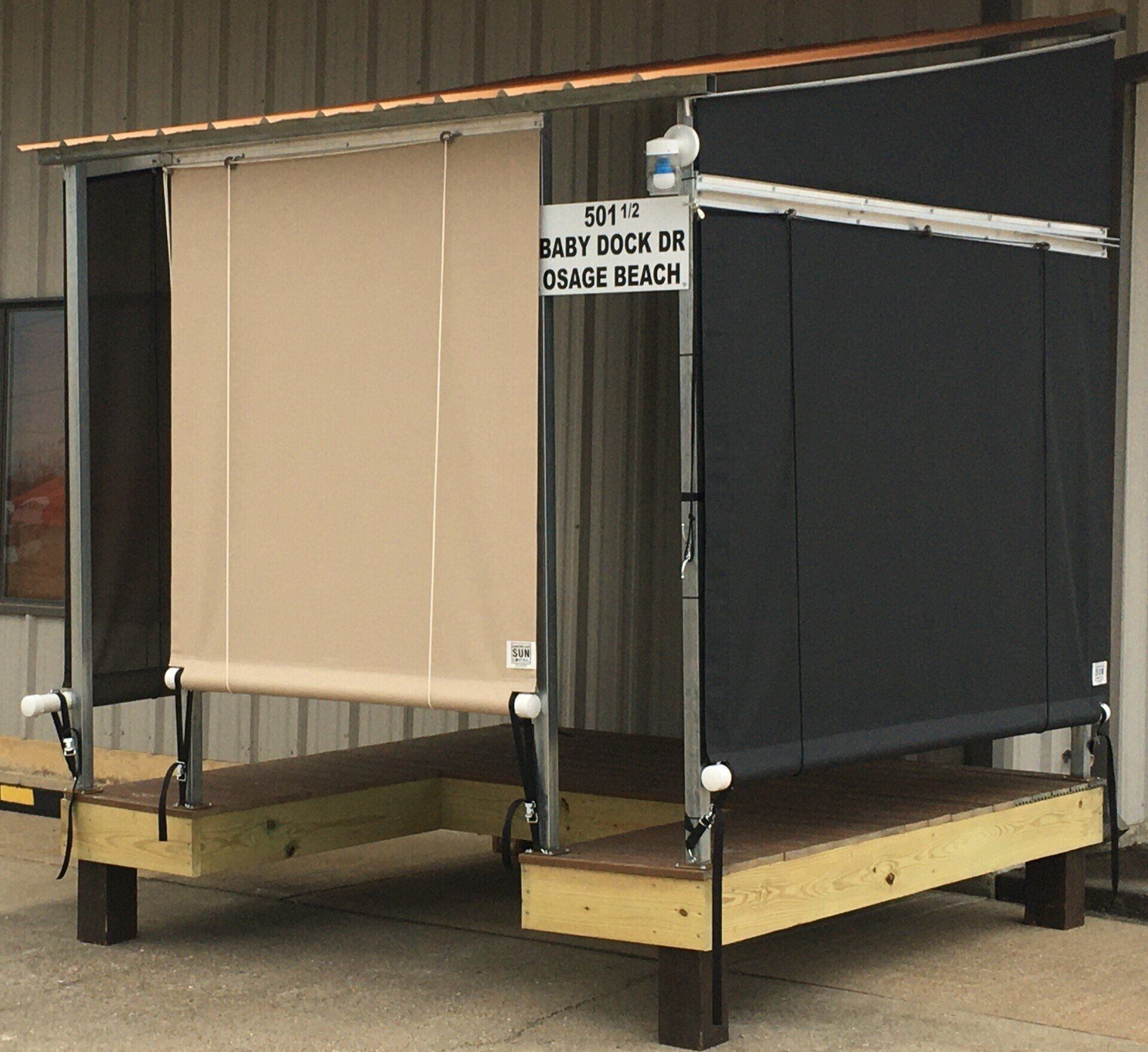 Two awning-style dock doors with beige and dark gray covers on a black metal frame, at a loading area.