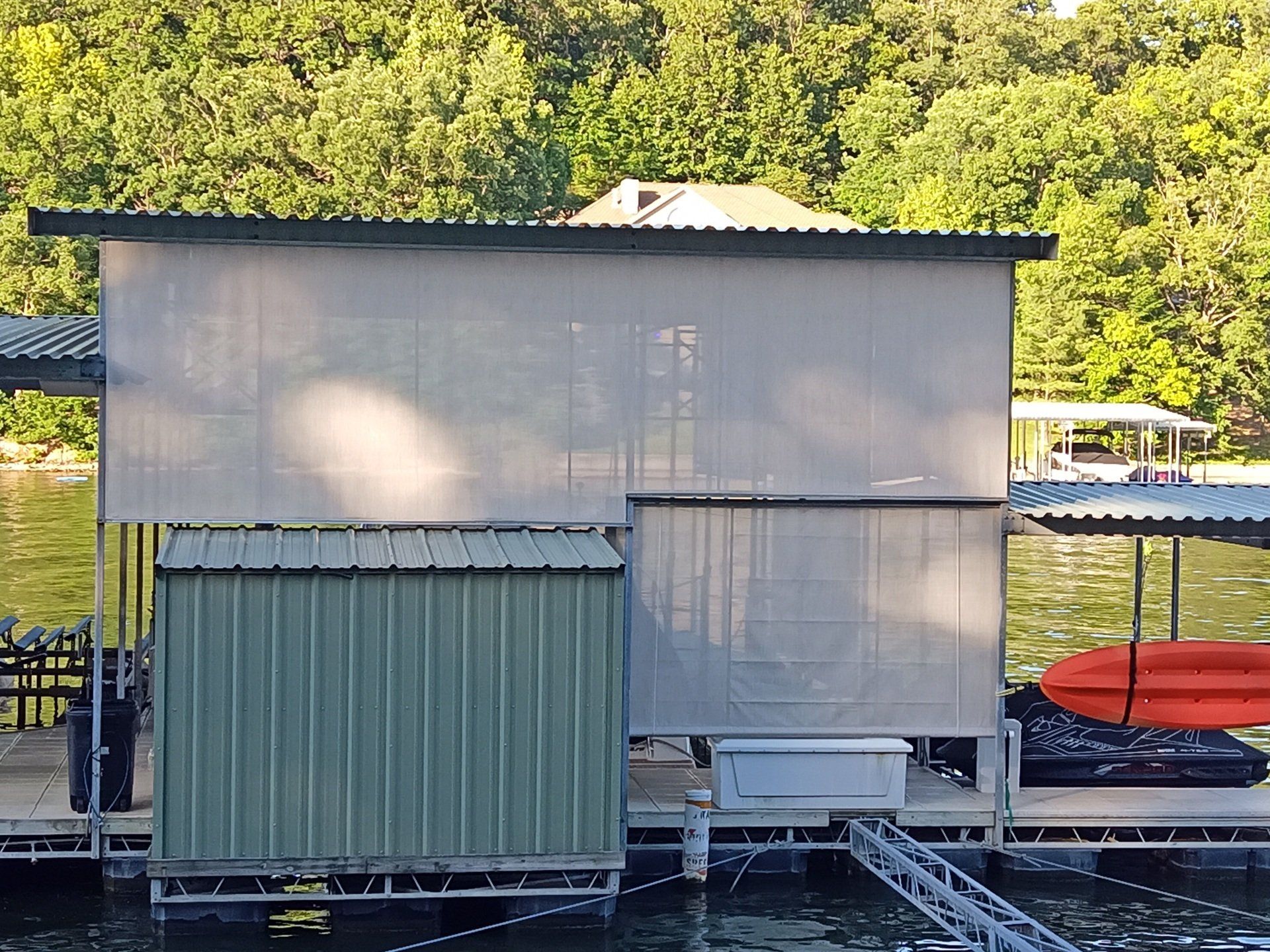 Small green shed-like structure with mesh siding and a red kayak on a rack beside it outdoors.