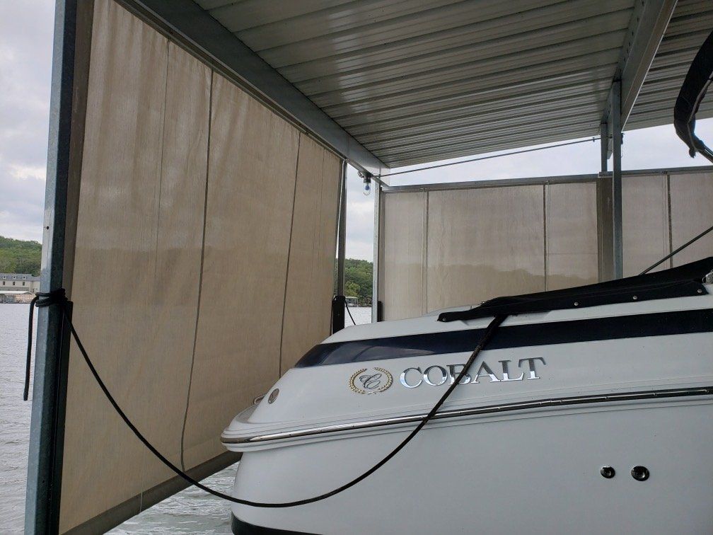 White boat under a covered dock with tan side curtains and a canopy roof
