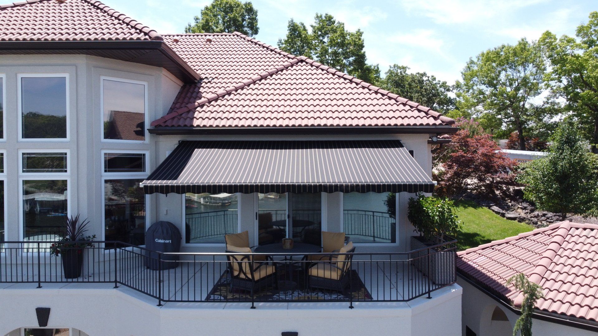 Balcony with patio furniture on a beige house with a red tiled roof under a black awning