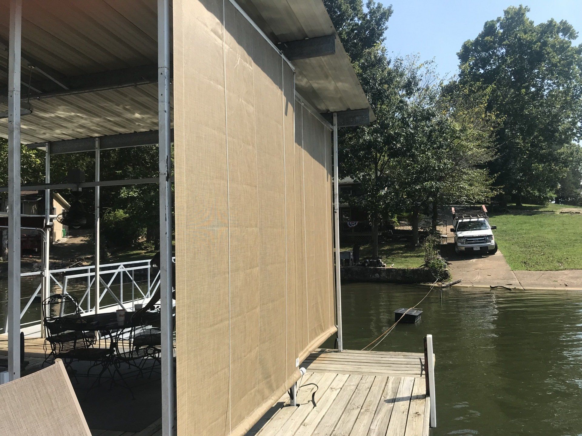 Covered dock beside a calm lake, with a tan wall, metal railing, and trees in the background
