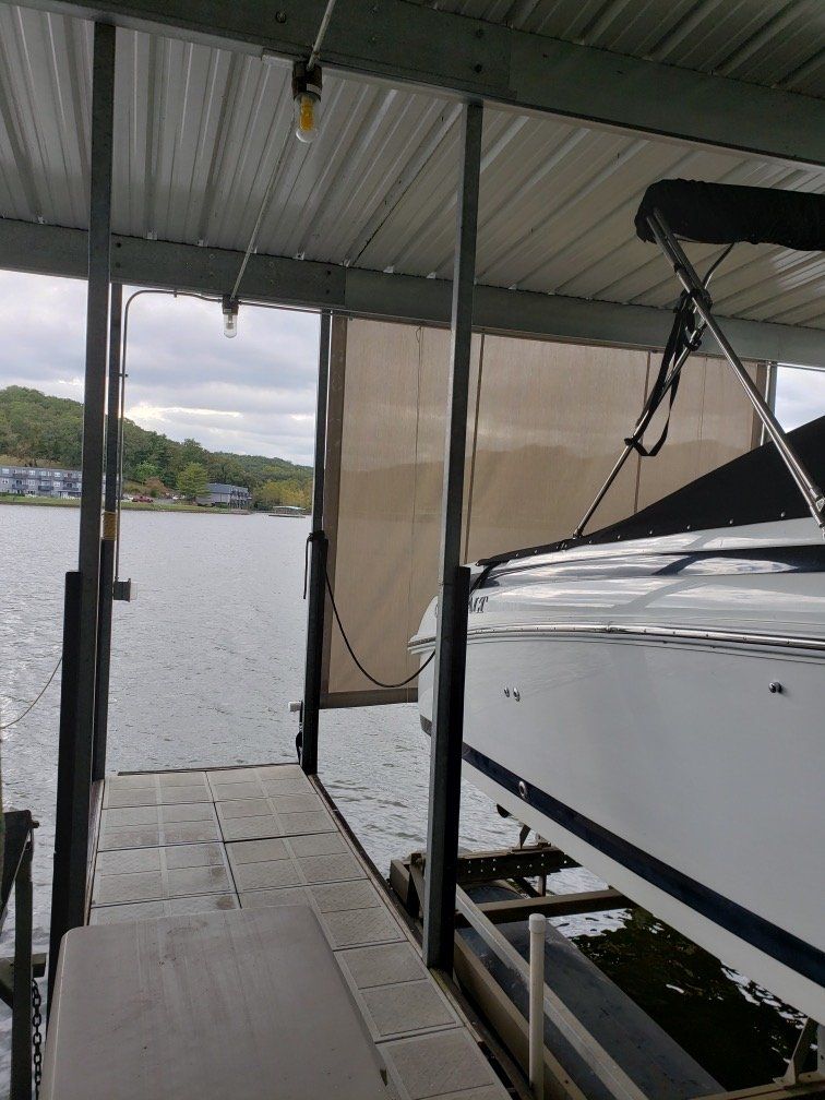Covered dock beside a white boat on calm water, with a concrete walkway and distant shoreline