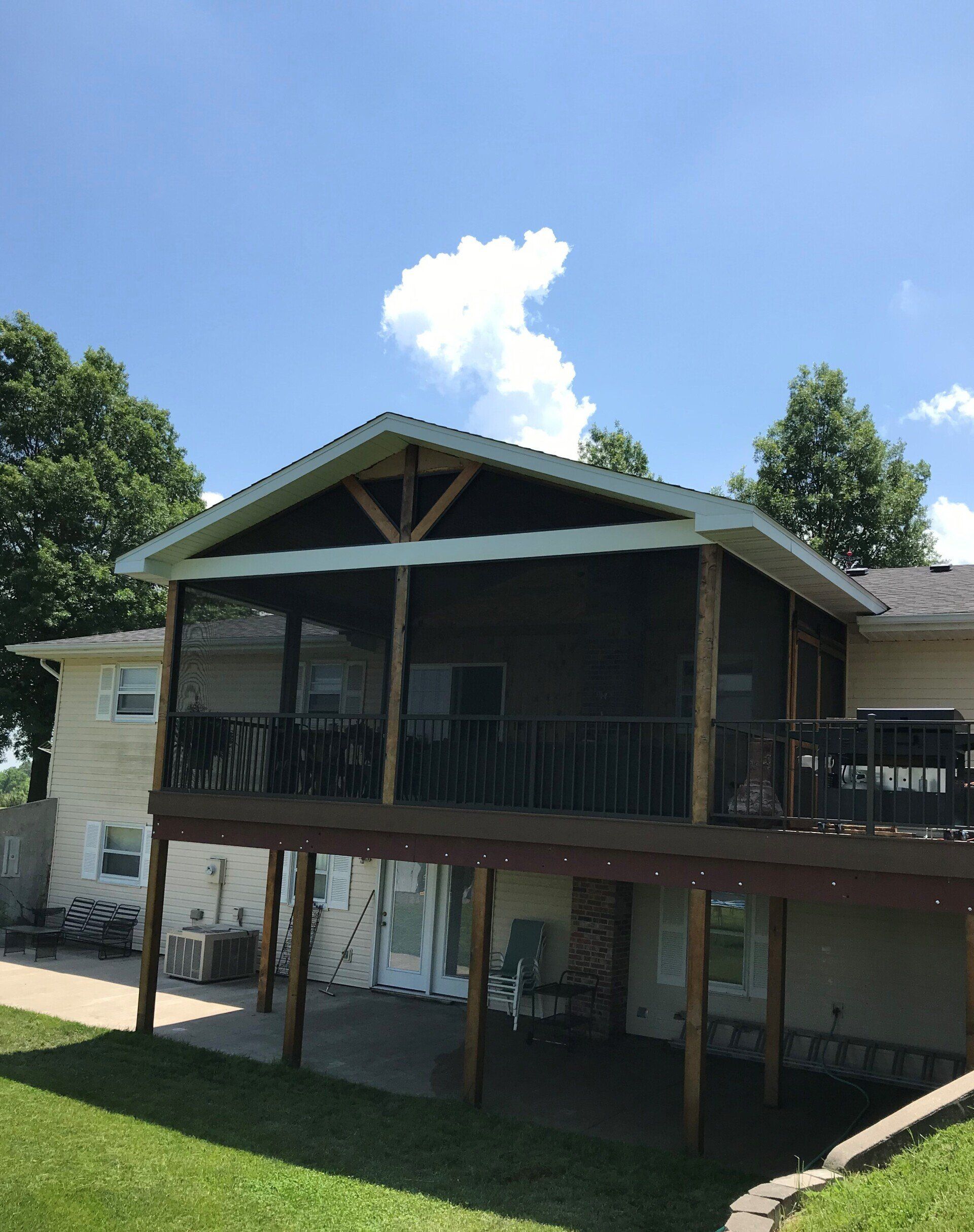 Two-story house with a screened porch and wooden balcony under a bright blue sky