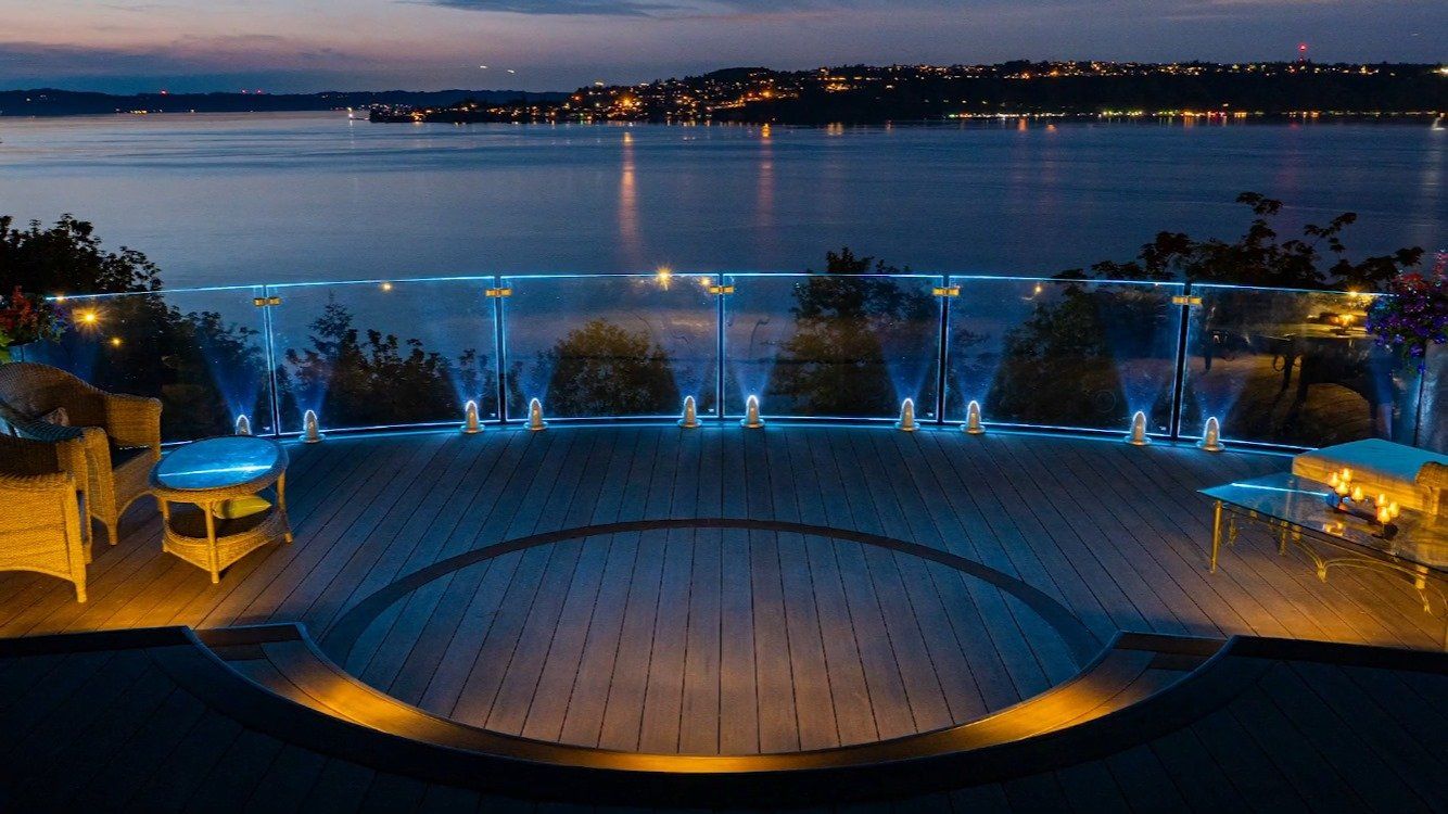 Nighttime waterfront terrace with blue-lit fountain, stone steps, and distant city lights across the water