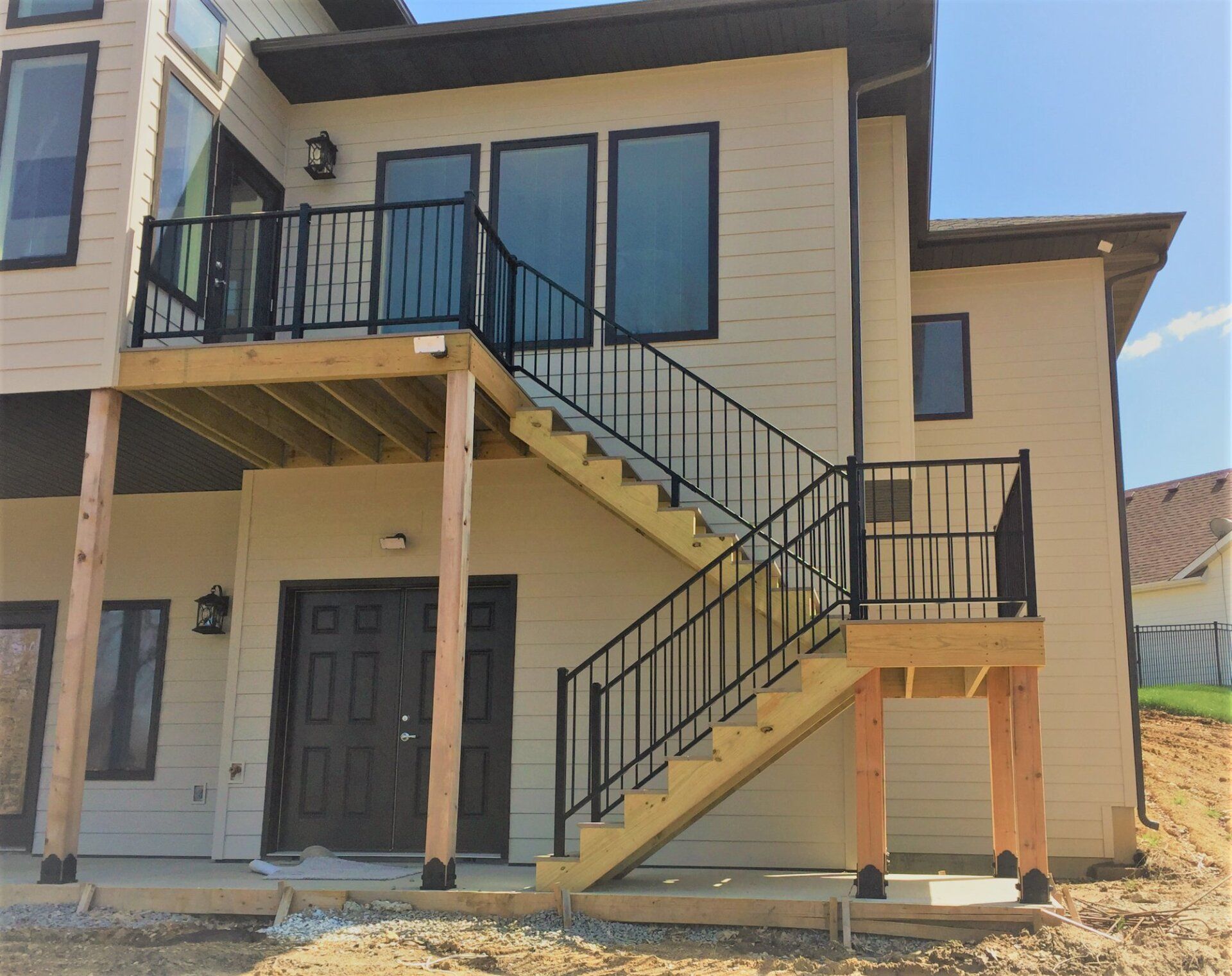 Two-story beige house exterior with black railings and an outdoor staircase leading to the second floor.