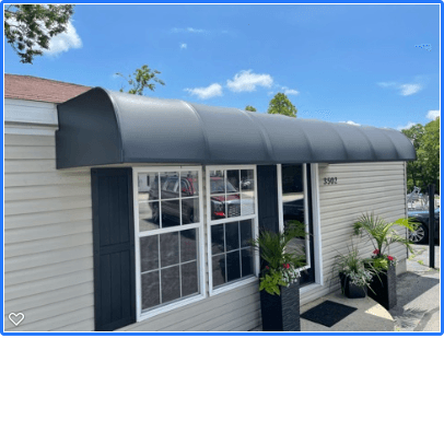 Small building entrance with gray awning, white siding, black trim, and potted plants under a blue sky