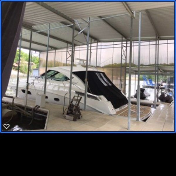White car under a metal carport, partially covered with a black tarp.
