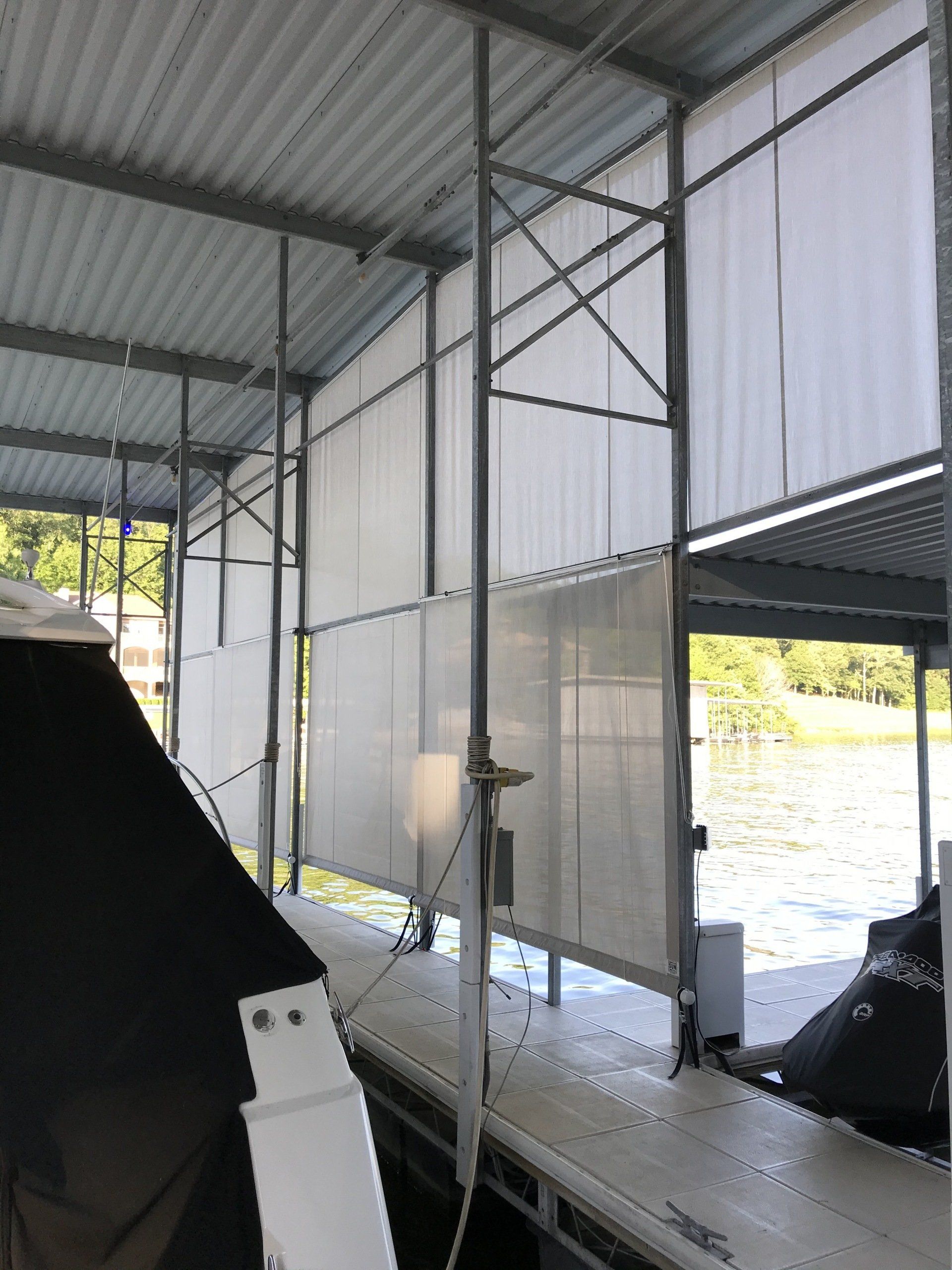 Covered dock with white mesh walls, metal roof, and a black boat on the water beside it