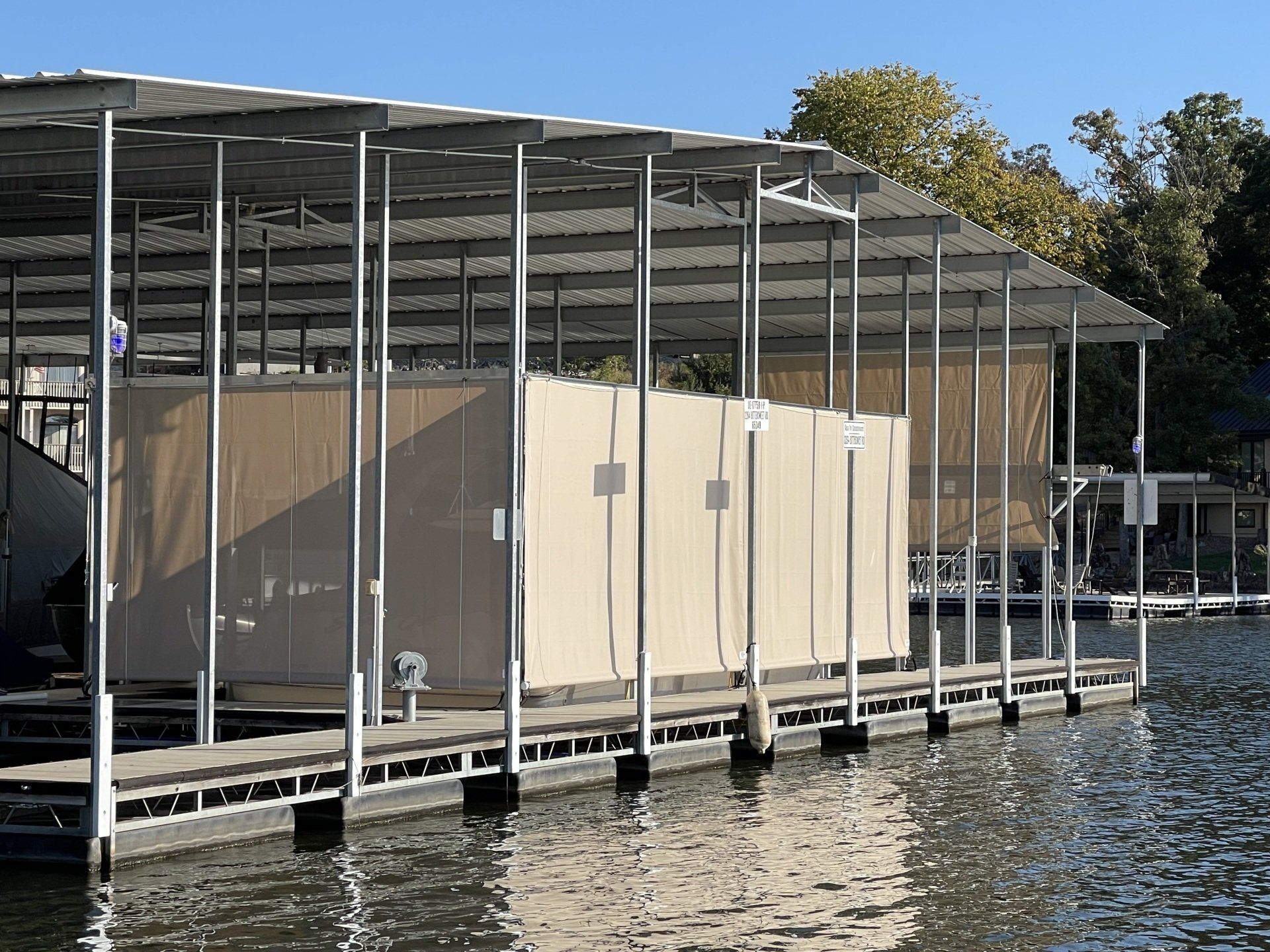 Covered dock with a beige storage shed over water, supported by metal posts.