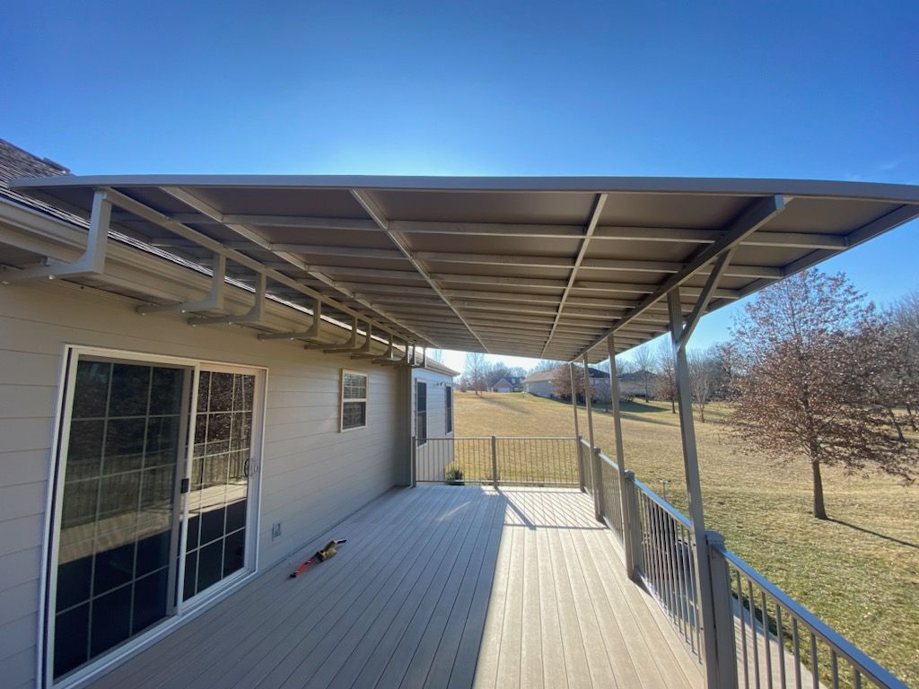 Covered wooden deck beside a house, with metal roof supports and a view of a grassy yard.