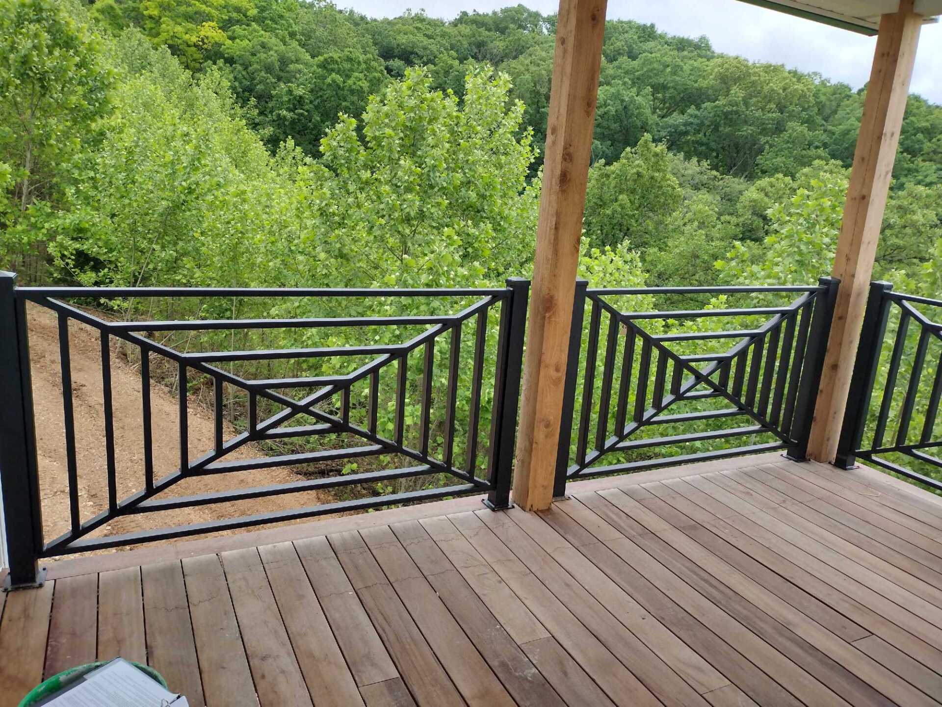 Wooden deck with black railings overlooking a green wooded hillside