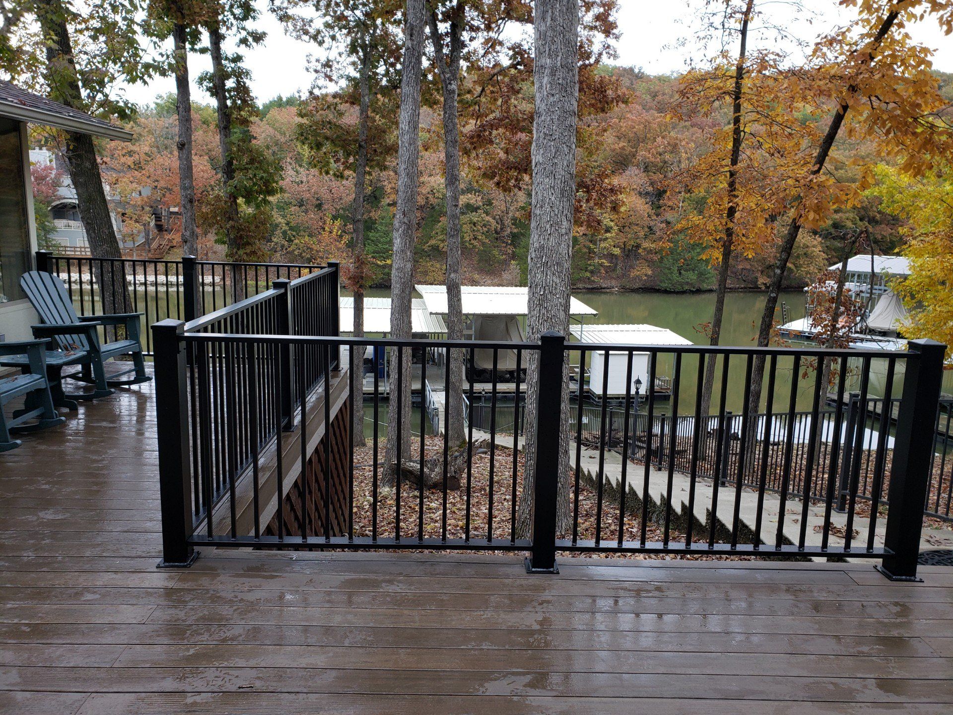 Wooden deck with black railings overlooking a calm lake and autumn trees