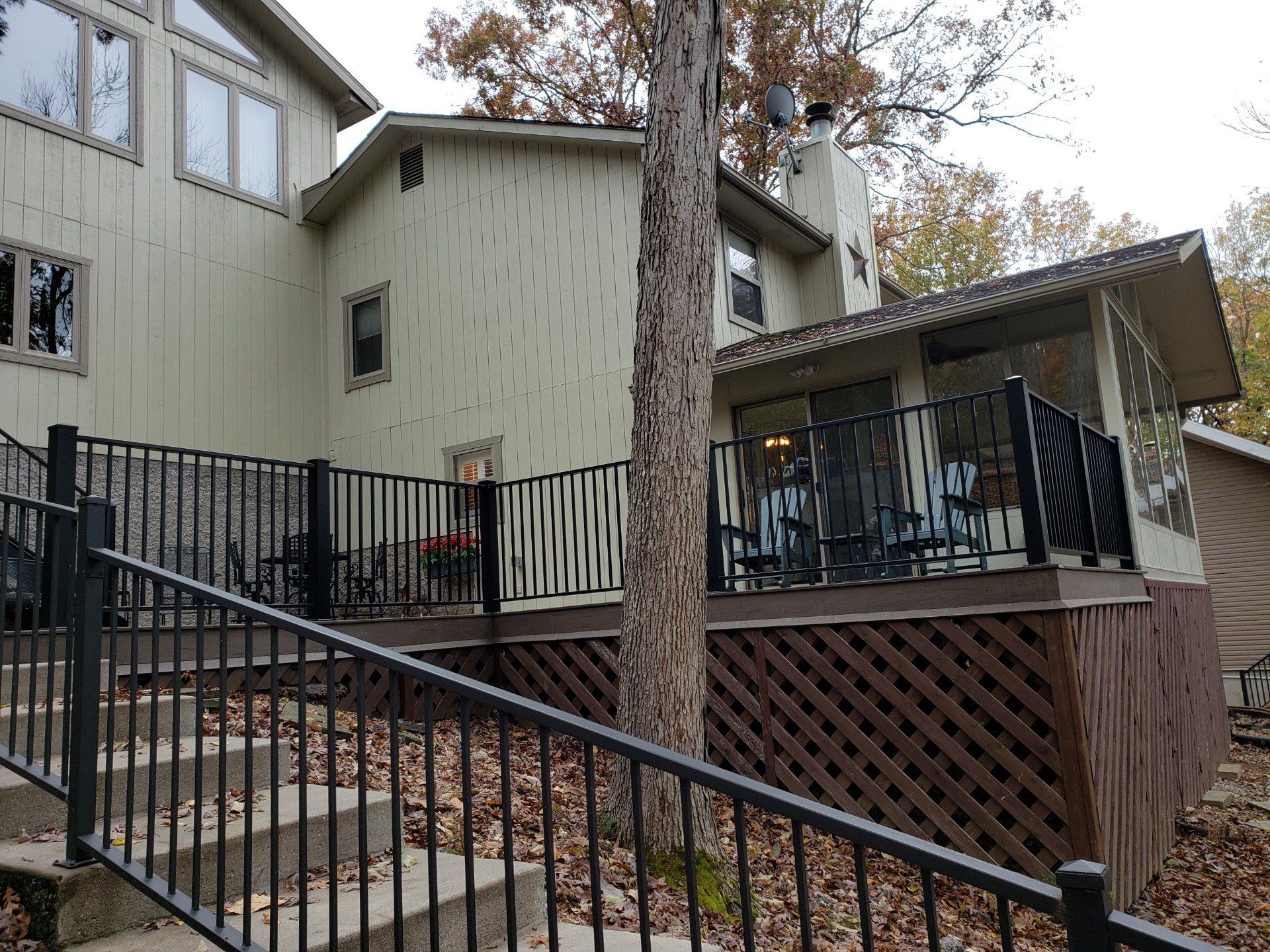 Wooden house deck with black railing, stairs, and autumn leaves on the ground