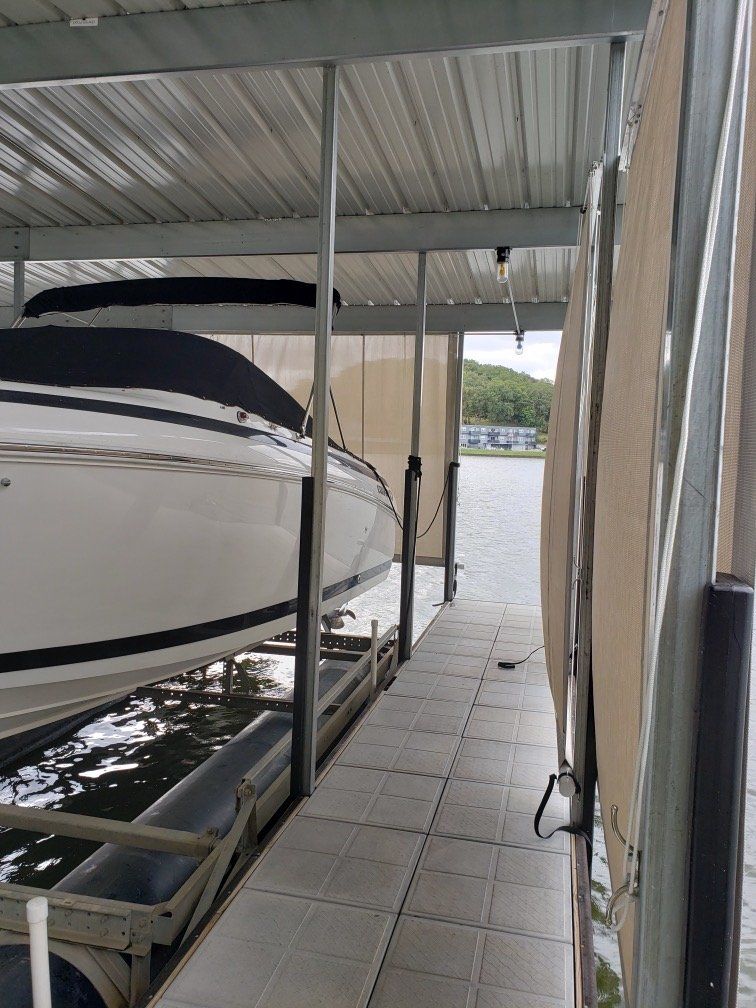 Covered boat slip with a white boat docked beside a tiled walkway and water view outside