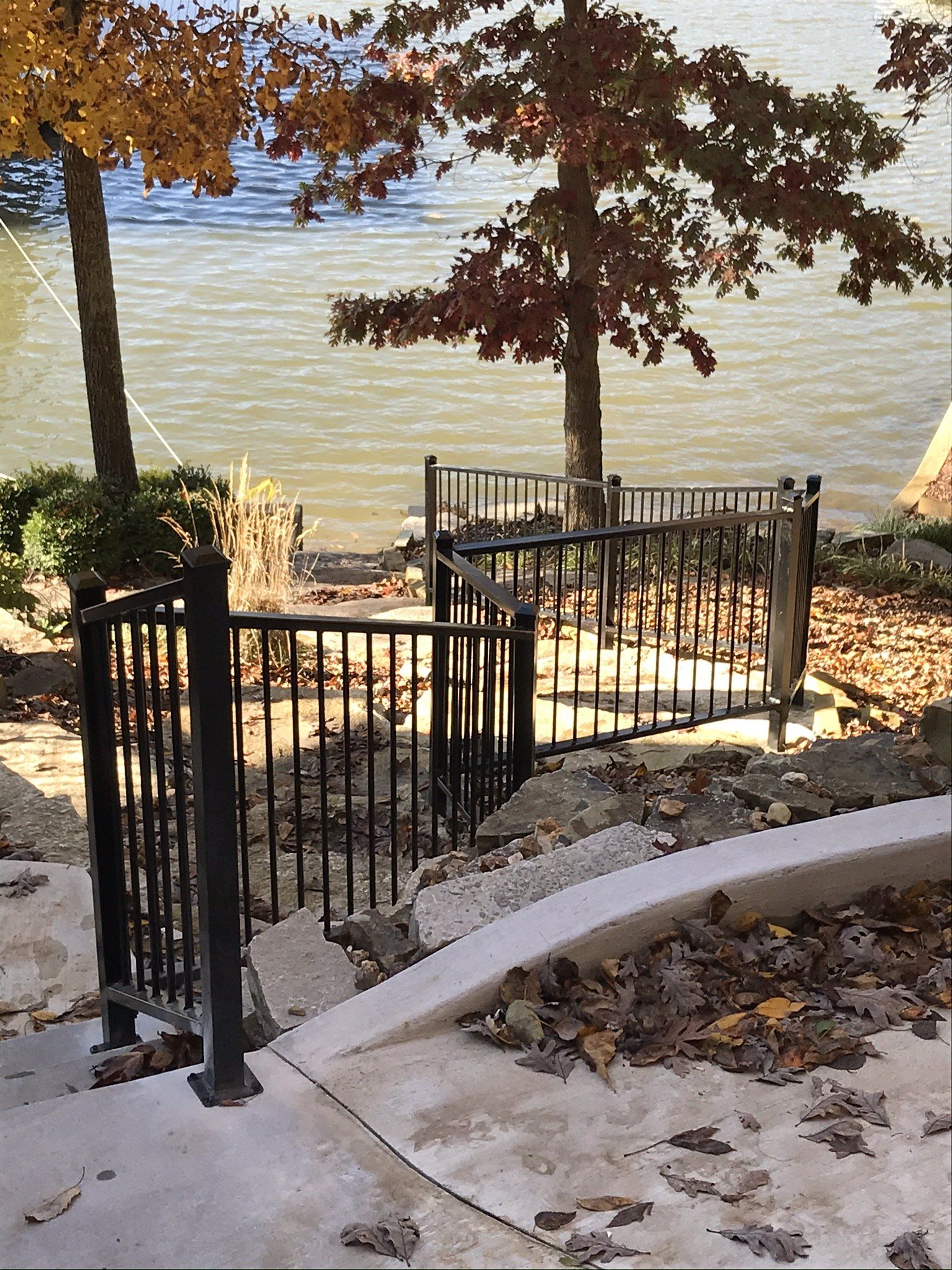 Stone steps with black railings leading down to a lakeside dock under autumn trees