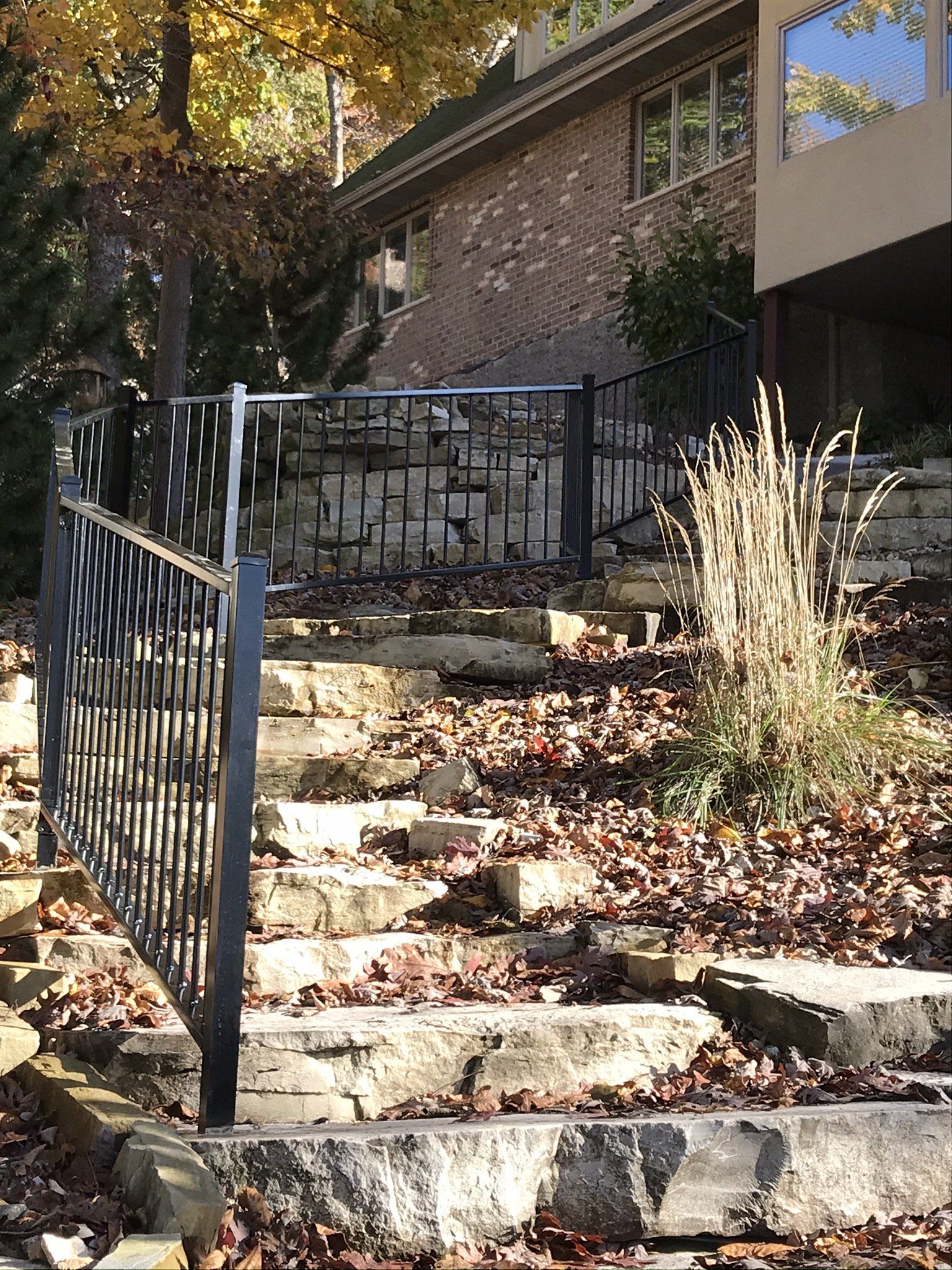 Stone steps with black iron railings leading up to a brick house in a wooded yard