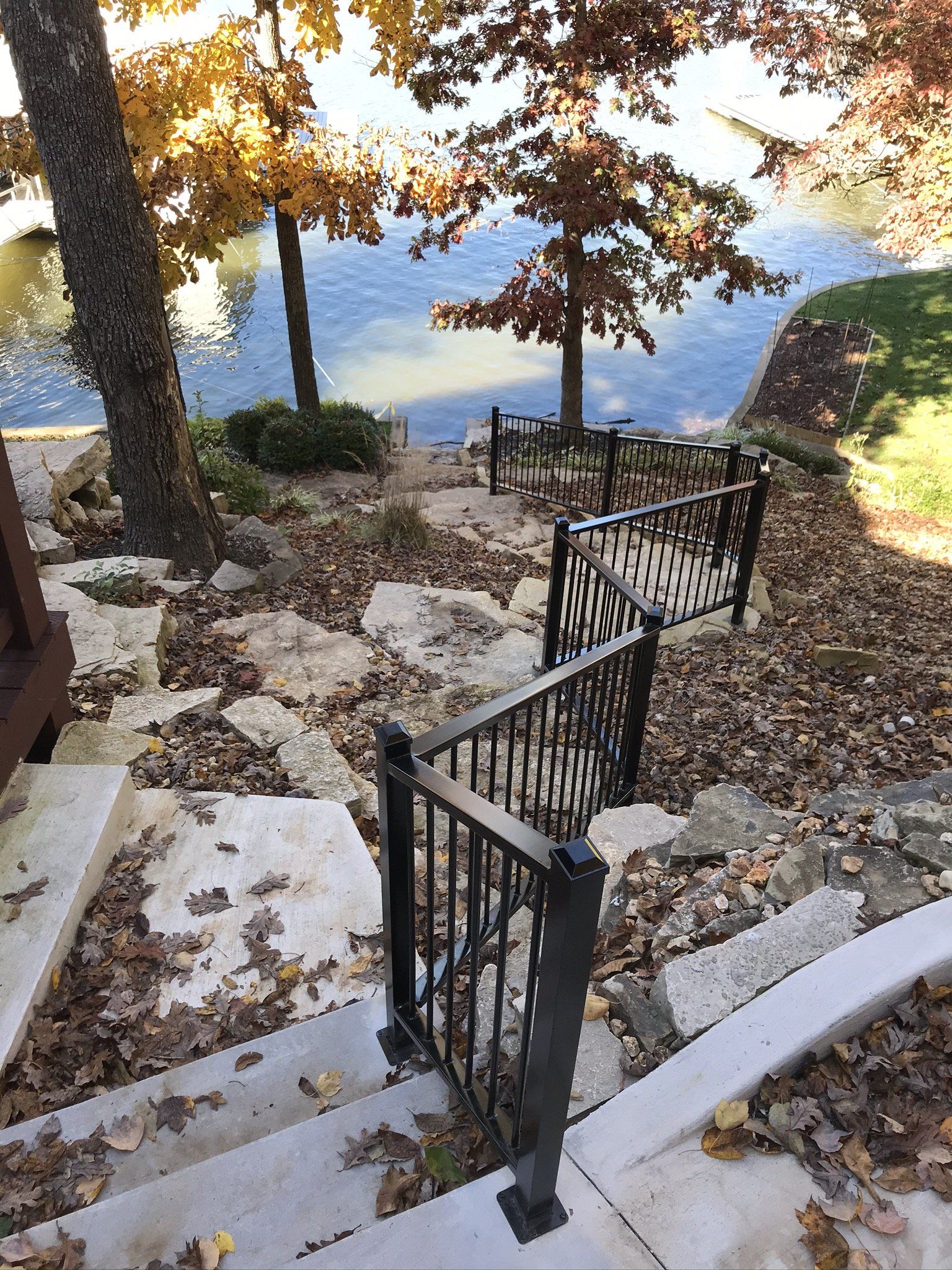 Stone steps and black railings descend through autumn trees toward a blue lake.