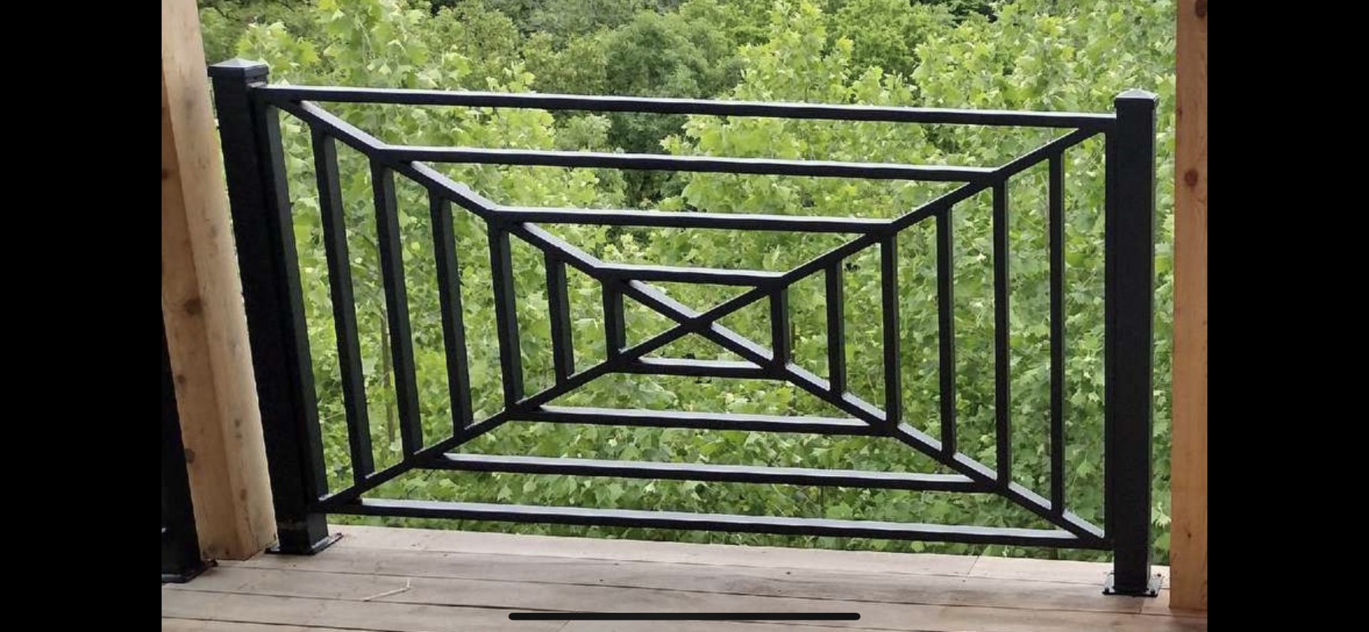 Black geometric railing on a wooden porch overlooking green grass