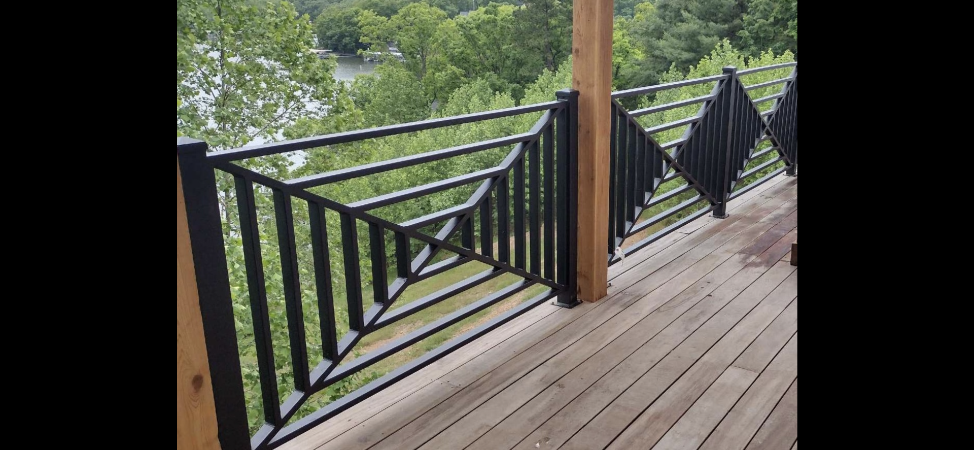 Wooden porch with black railings overlooking lush green trees and a hillside