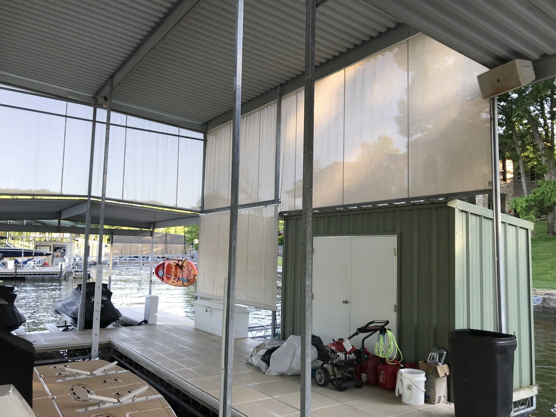 Covered outdoor storage area with metal roof, wet floor, stacked bags, and cleaning supplies beside a white container