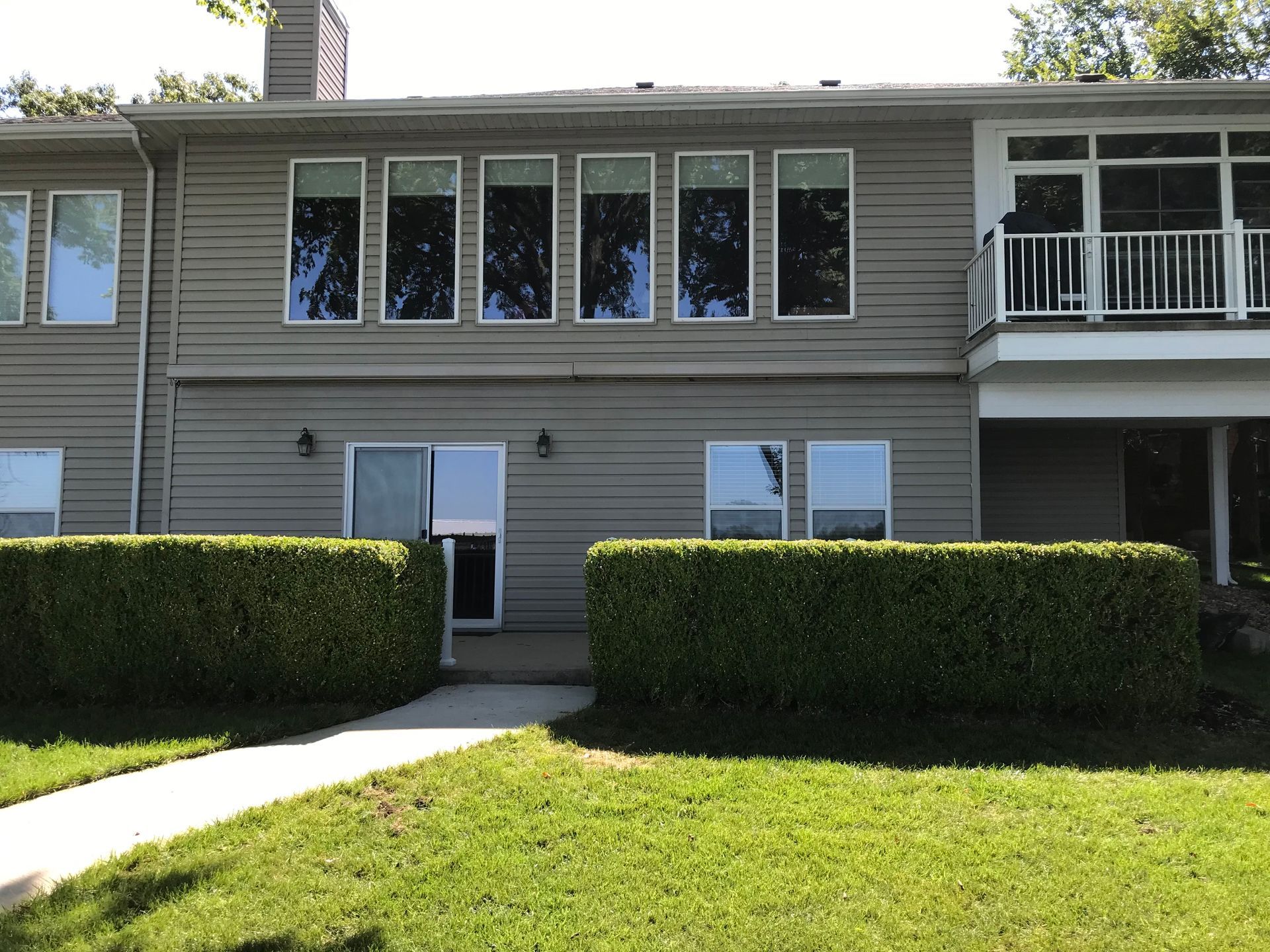 Two-story apartment building with white trim, hedges, and a grassy walkway in front