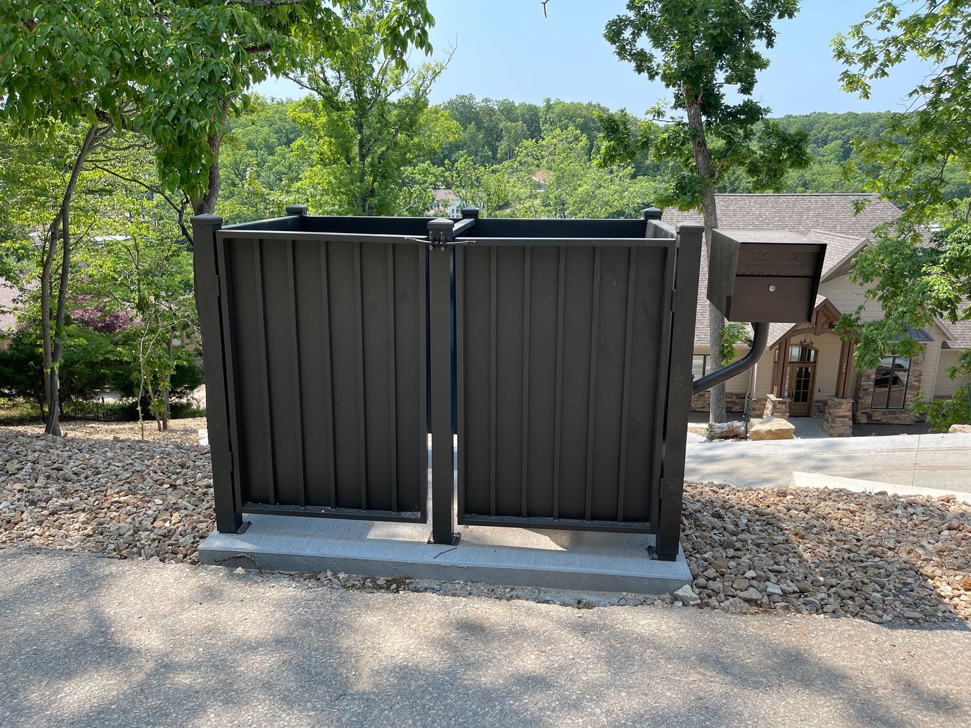Black metal gates on a gravel path in a leafy outdoor garden setting