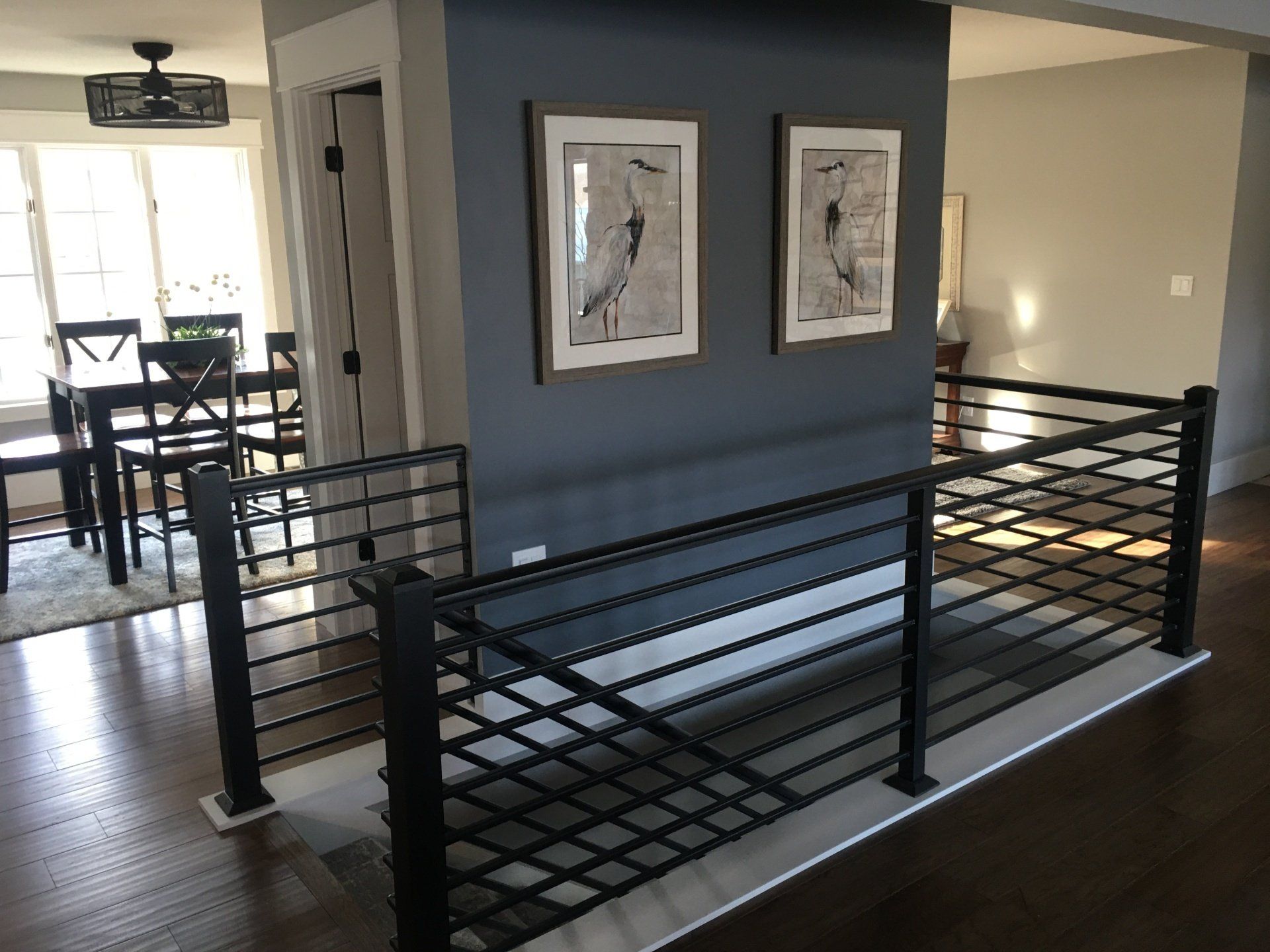 Modern home interior with black metal stair railing and wall art near a dining area.