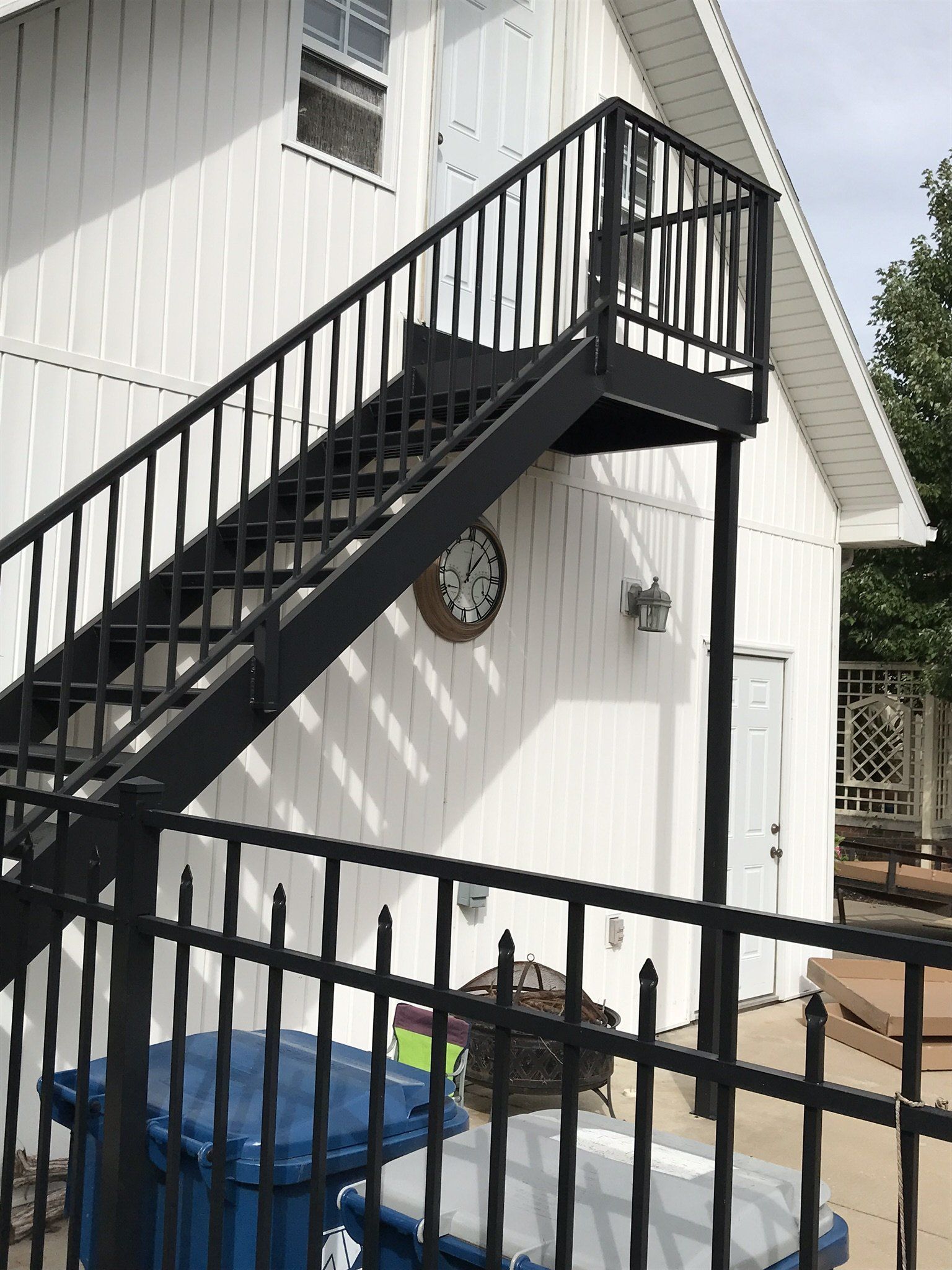 Black metal staircase and landing on the side of a white house with an outdoor patio below