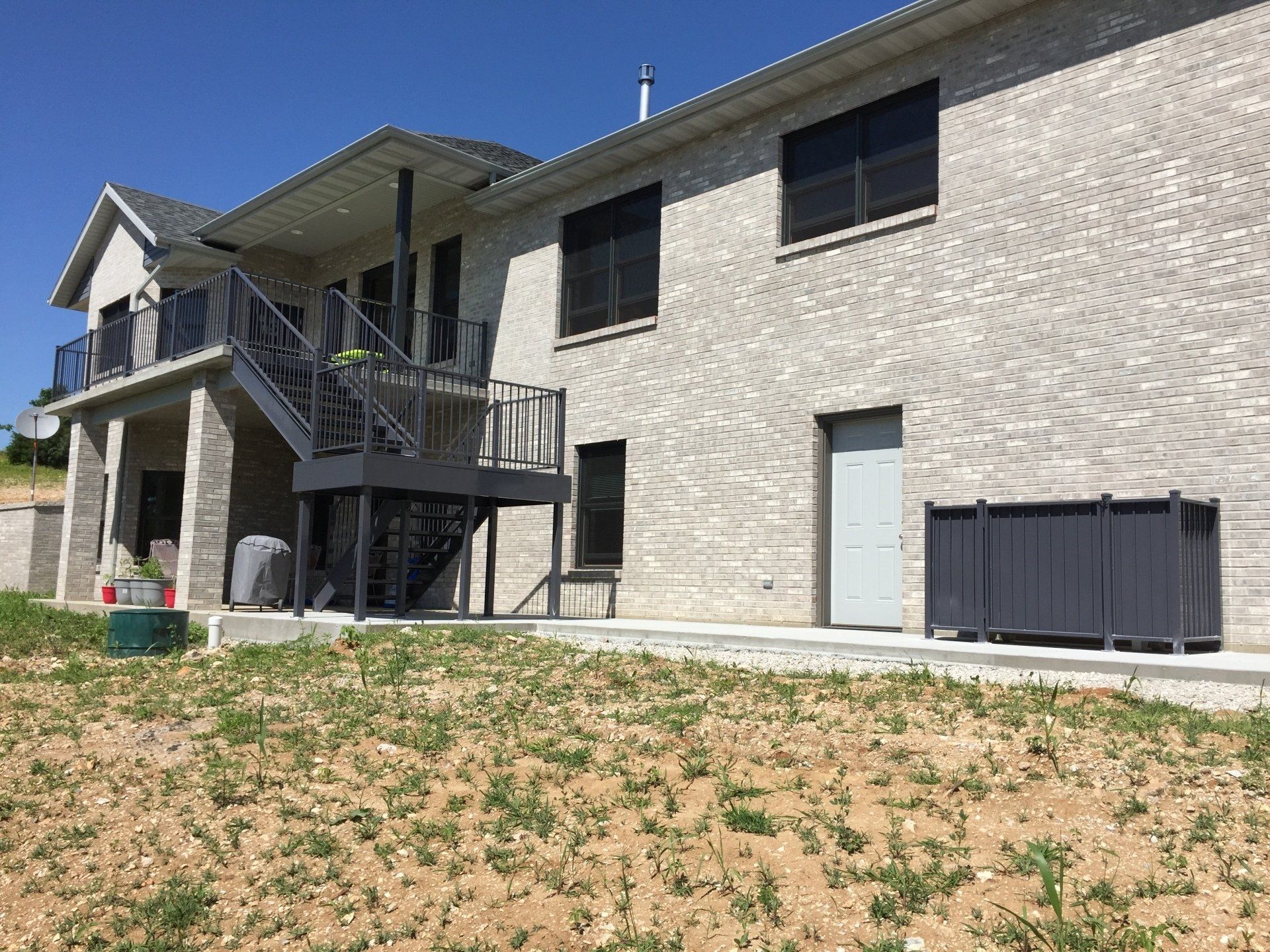 Brick apartment building with exterior stairs, balconies, and a grassy yard under a blue sky