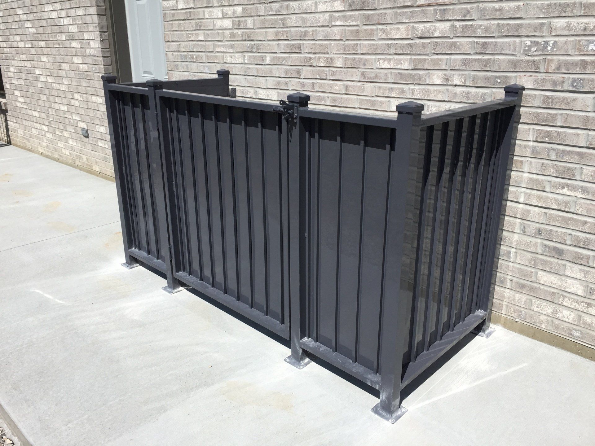 Black metal railing enclosure on a concrete walkway beside a brick wall.