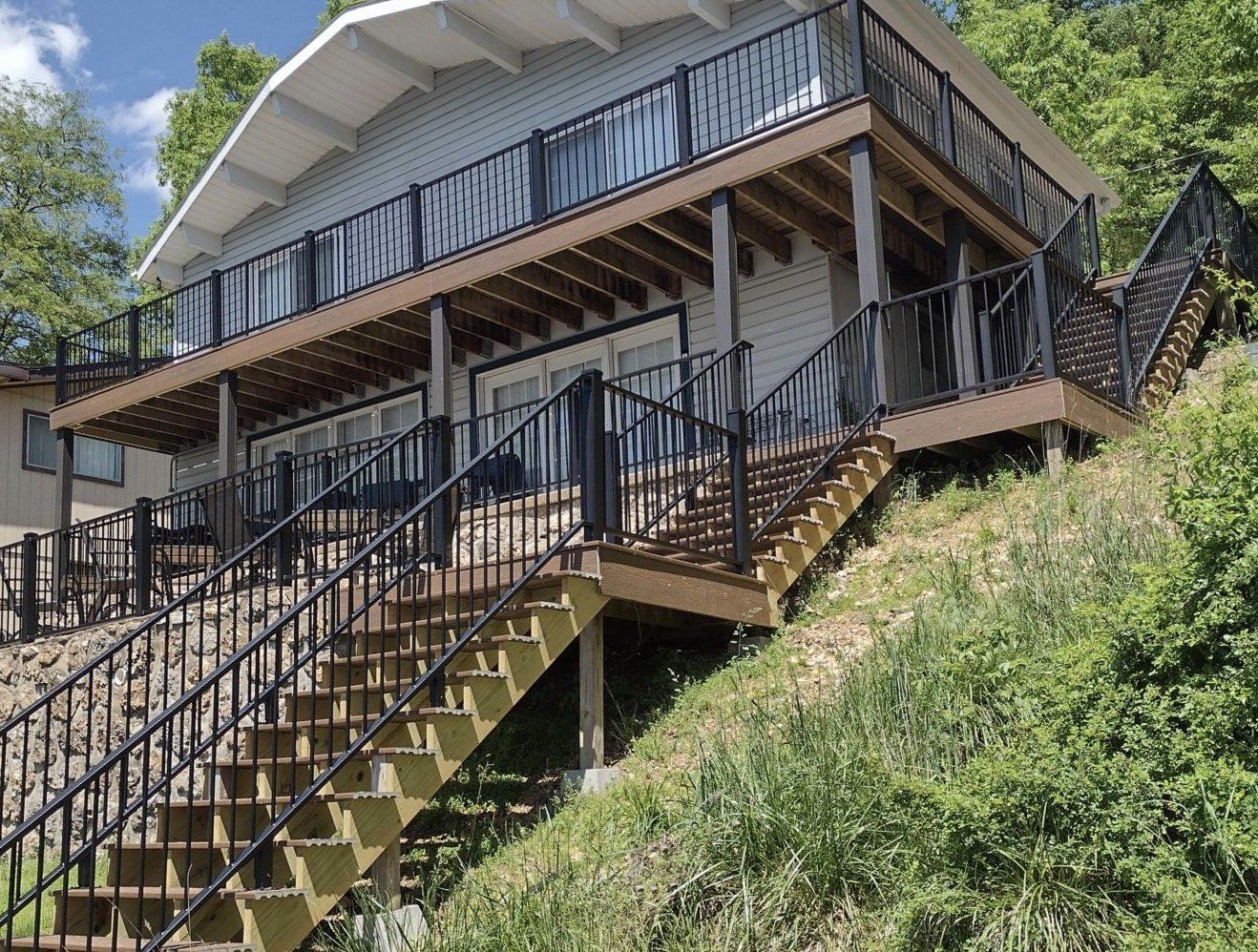 Modern hillside house with black staircases and railings, surrounded by green vegetation