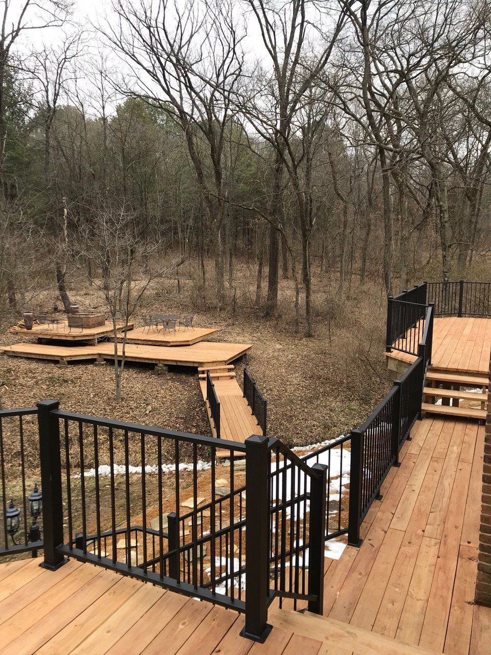 Wooden boardwalk and deck with black railings overlooking a leafless wooded area