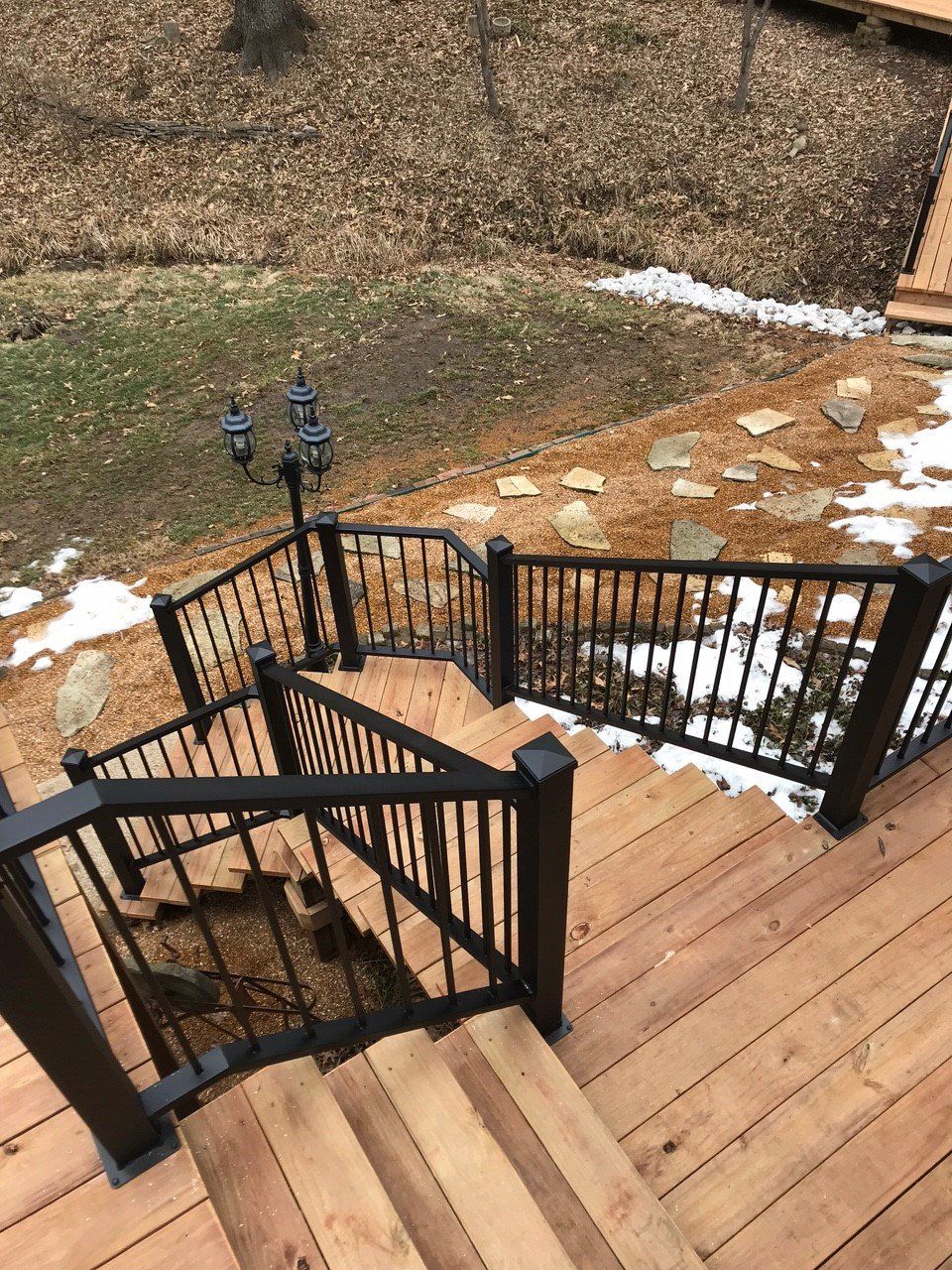 Wooden deck stairs with black railings descending to a snowy yard and stone path.